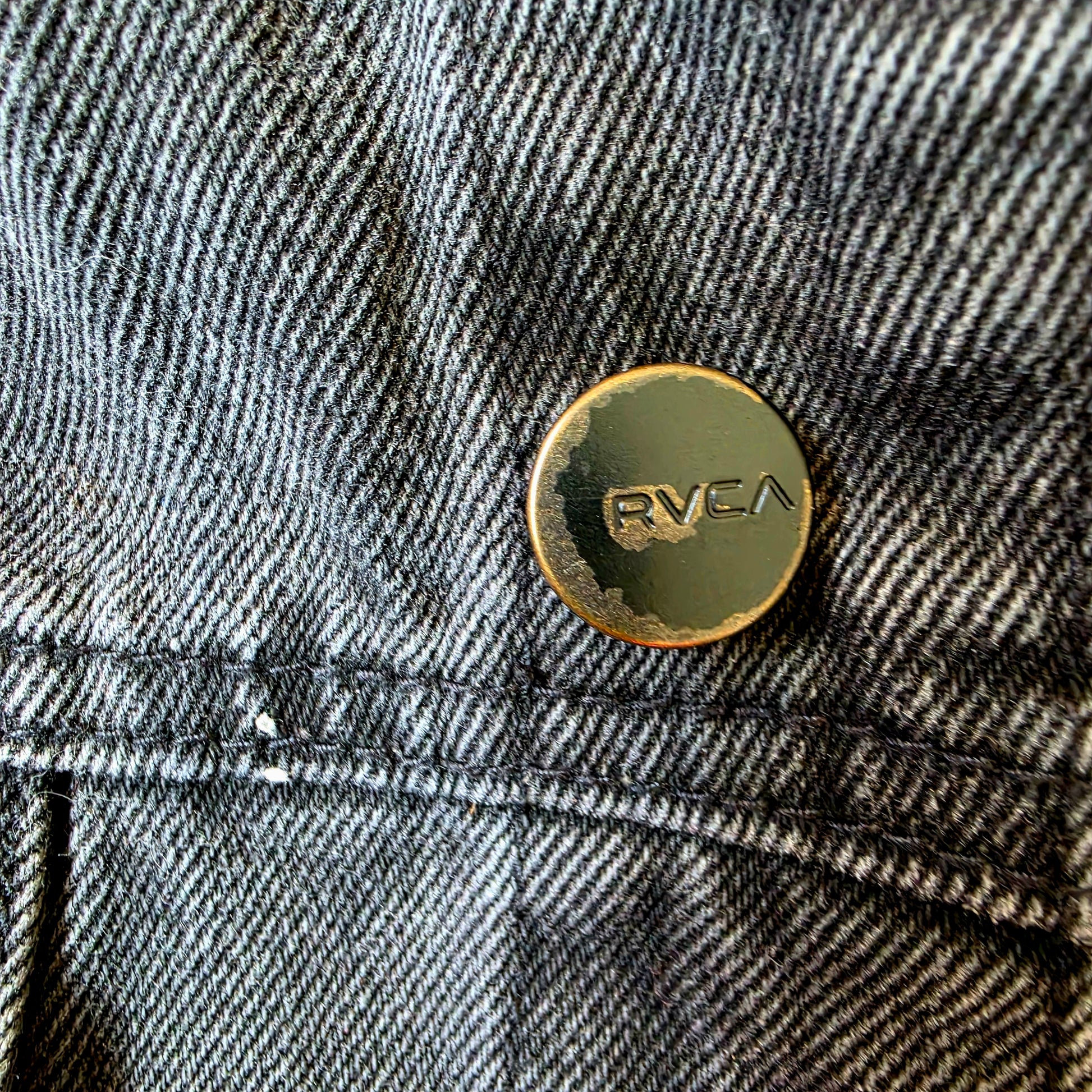Close-up of a denim jacket wit showing wear and tear of the button featuring the brand 'Rvca' 