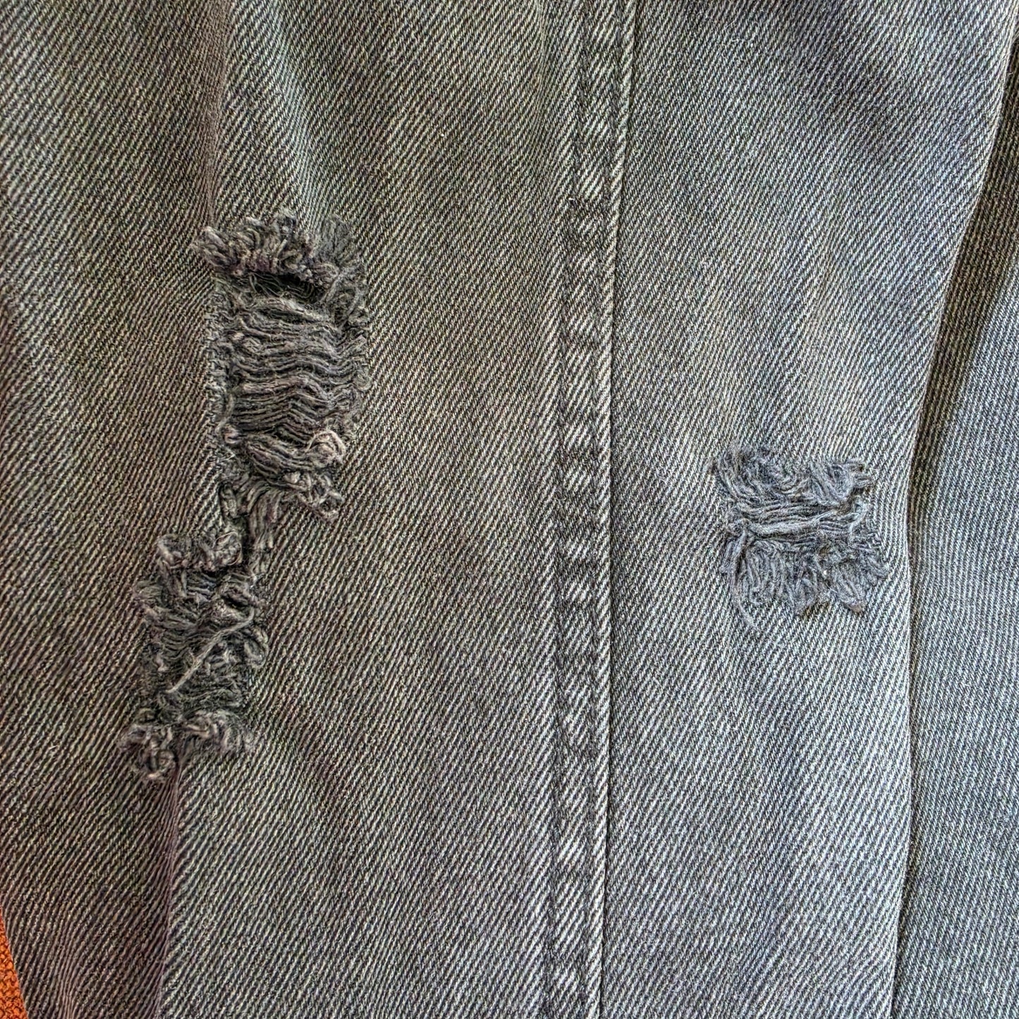 Detailed view of faded black denim texture with natural wear and factory distressing on sleeves