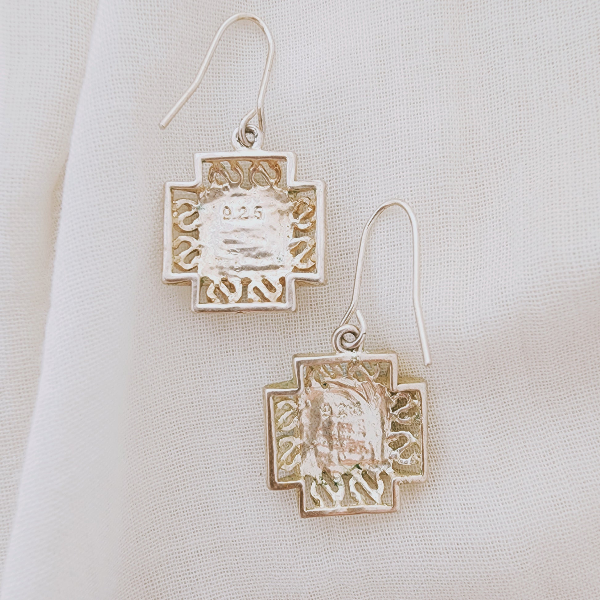 The back view of sterling silver earrings with turquoise-coloured stones in a square setting, photographed on soft neutral fabric.