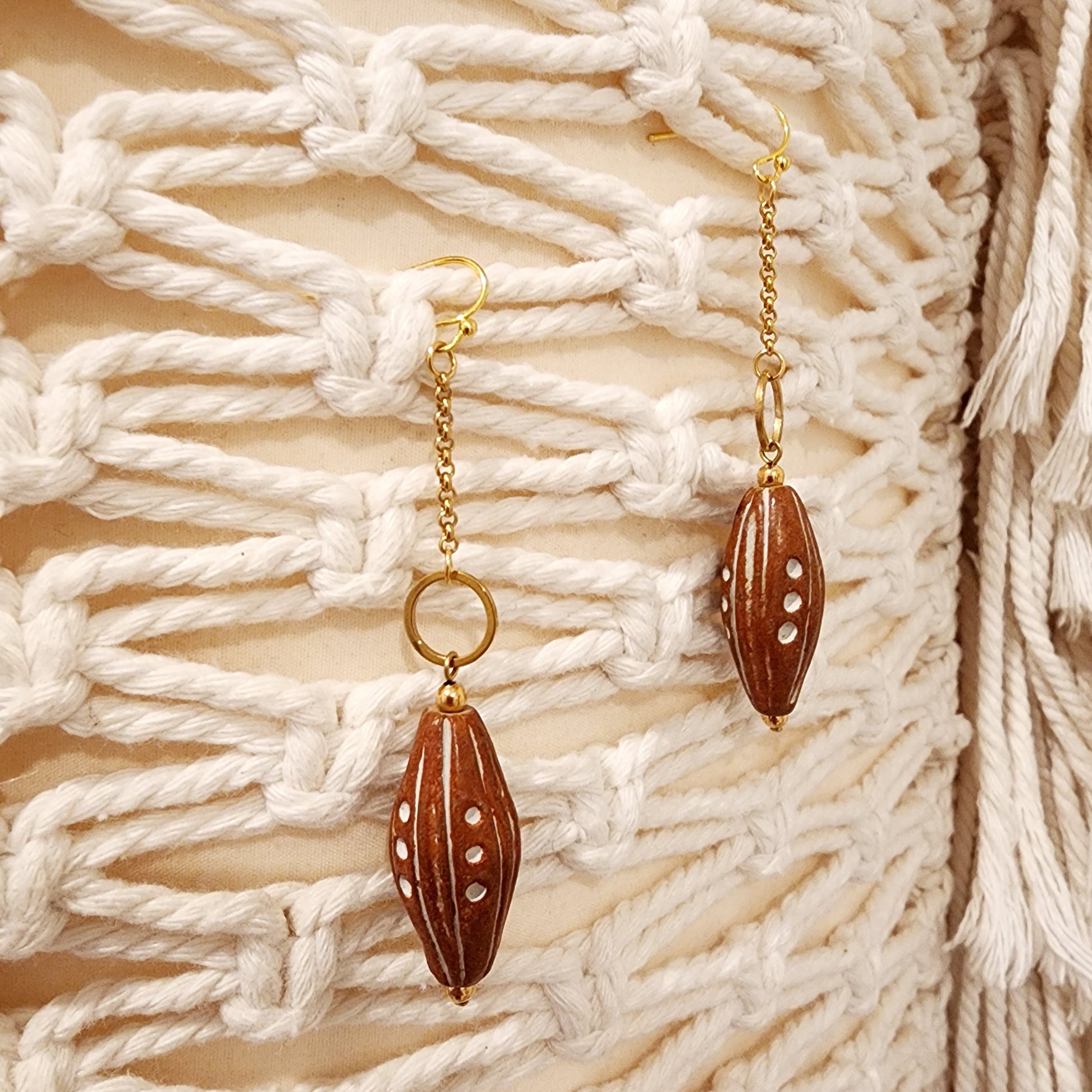 Front view of The Ramblers handmade earrings featuring long recycled clay beads and gold-plated stainless steel hooks on a macramé backdrop.