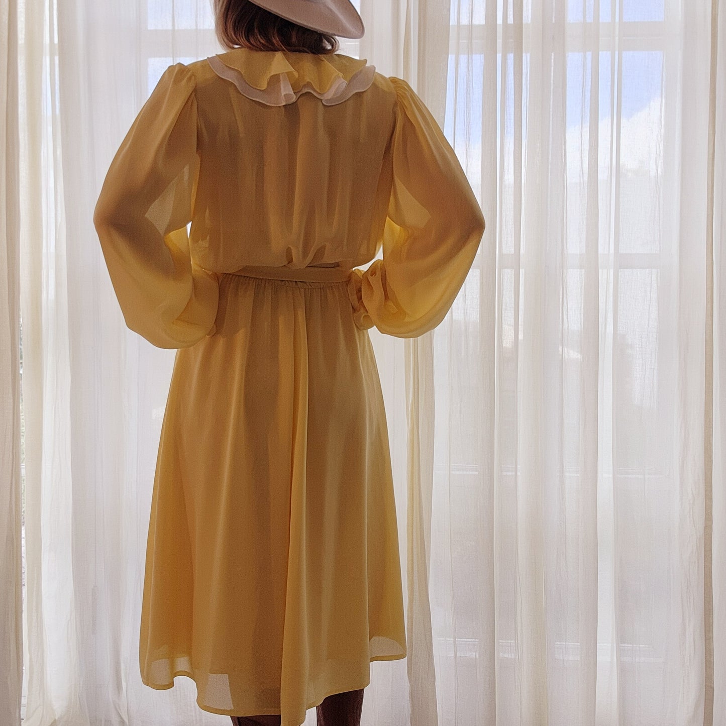 Back view of model wearing the Vintage Peter Barron Dress, showing the semi-sheer lemon colour with a ruffle neckline, tie belt and soft sleeves.