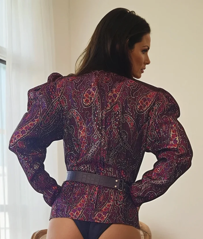Model showing the back of vintage purple metallic paisley top, showing the zip up back, puff shoulders and longer sleeves.