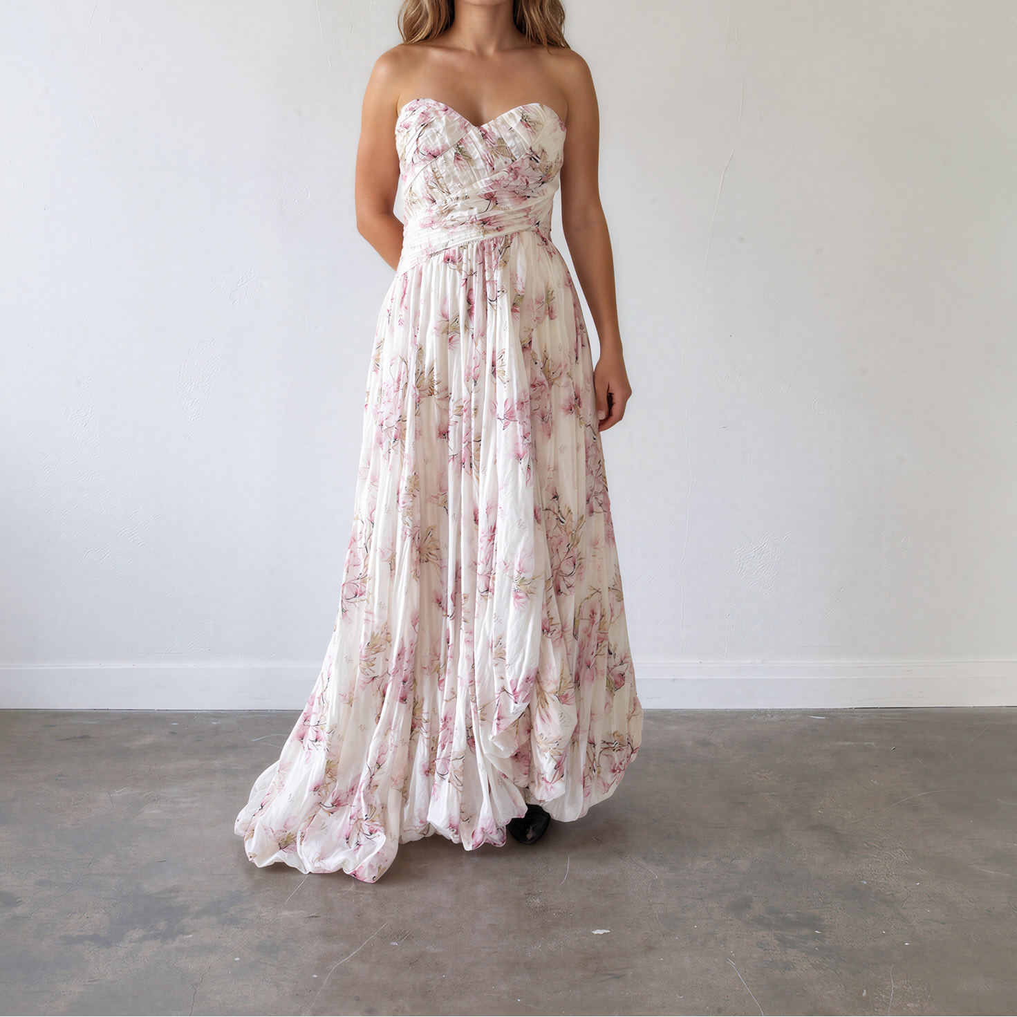 A woman showing the front view of the Aje strapless maxi dress with a sweetheart neckline, a fitted waist, and a flowing skirt with a pink floral print on a cream background.