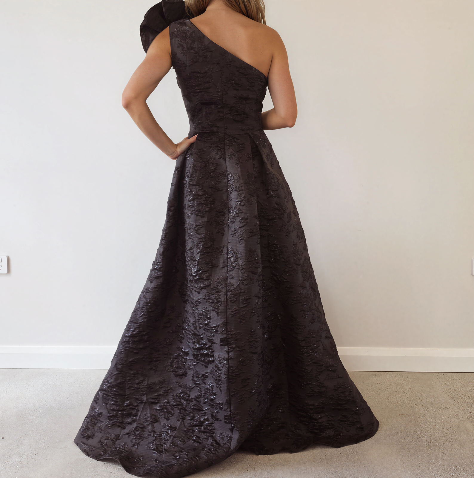Back view of the Anissa one-shoulder black jacquard evening gown featuring an asymmetric neckline, fitted bodice and sweeping full skirt.