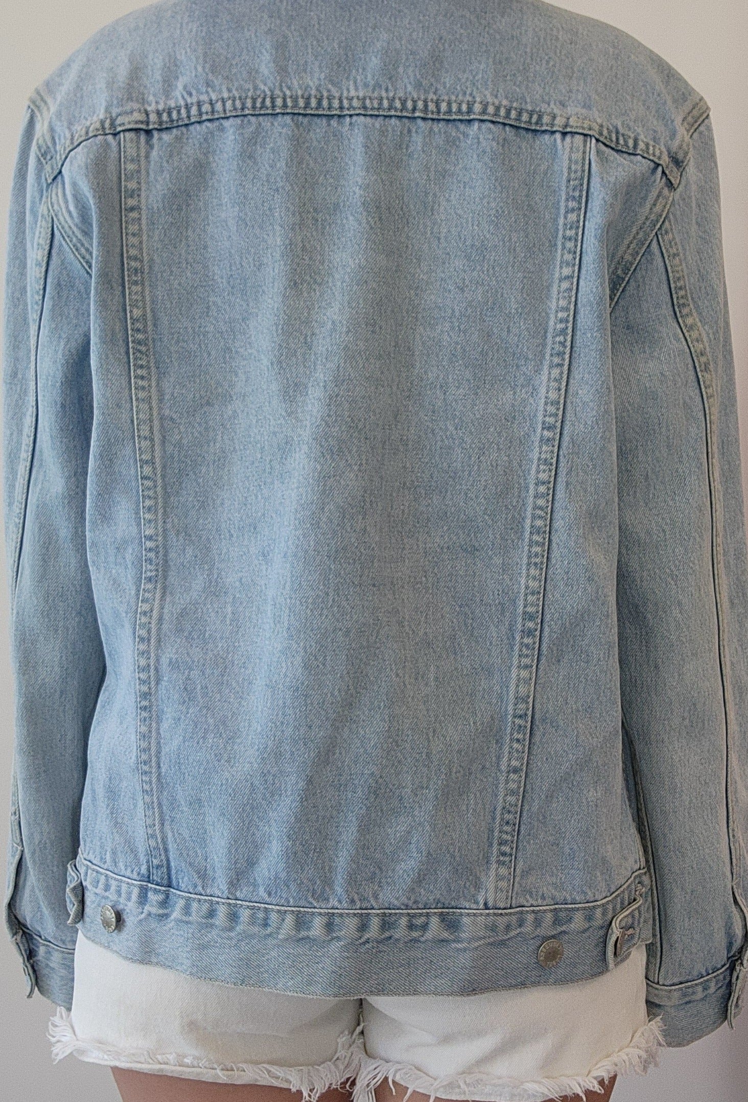 Close-up view of the back of the Assembly Label denim jacket, showing the back adjustable panels and light wash denim.