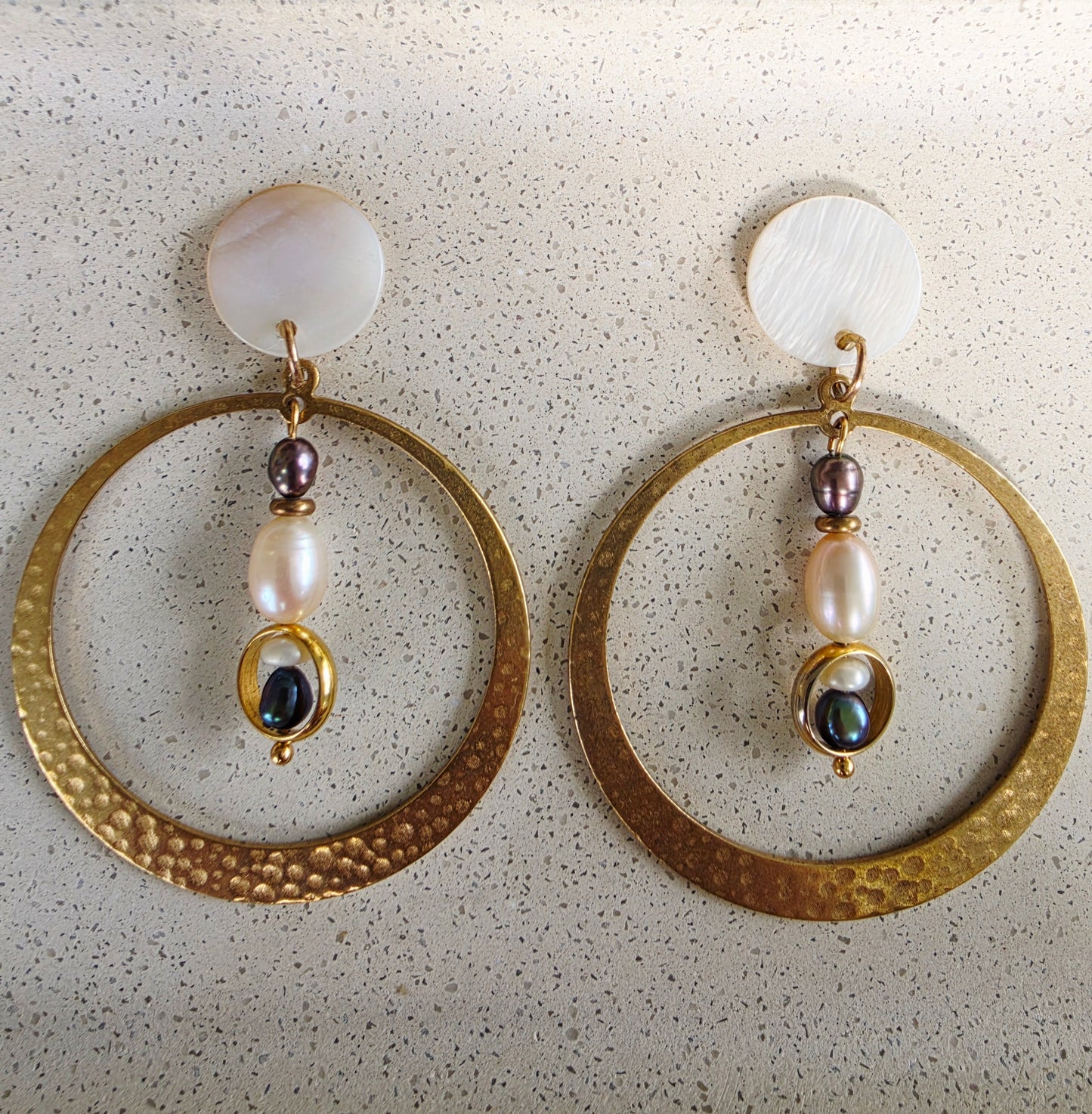 Close up vies of the Auricle pearl hoop earrings, showing the hammered brass hoop, mixed hanging pearls and mother of pearl components.