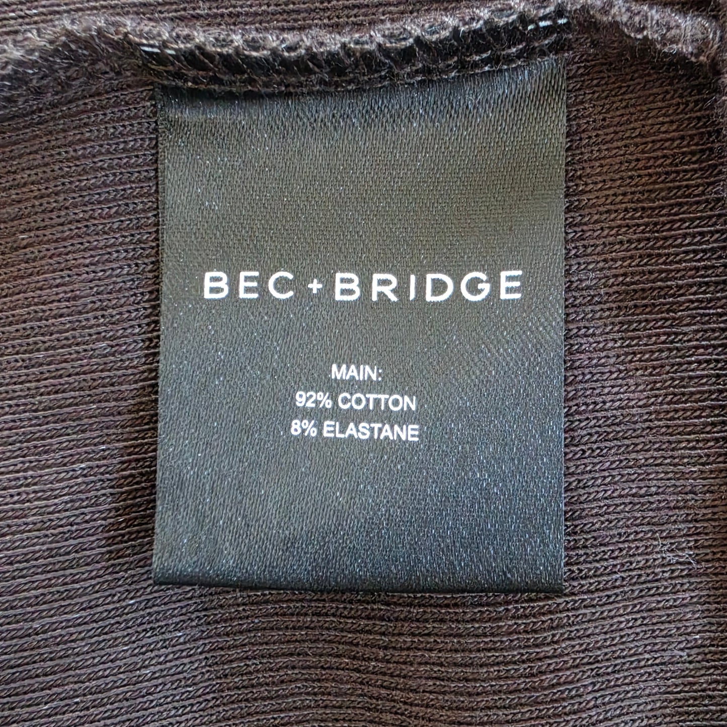Close-up of the dark chocolate Bec & Bridge Kody Ribbed mini dress, with label reading BEC+BRIDGE, with text specifying 92% cotton and 8% elastane.