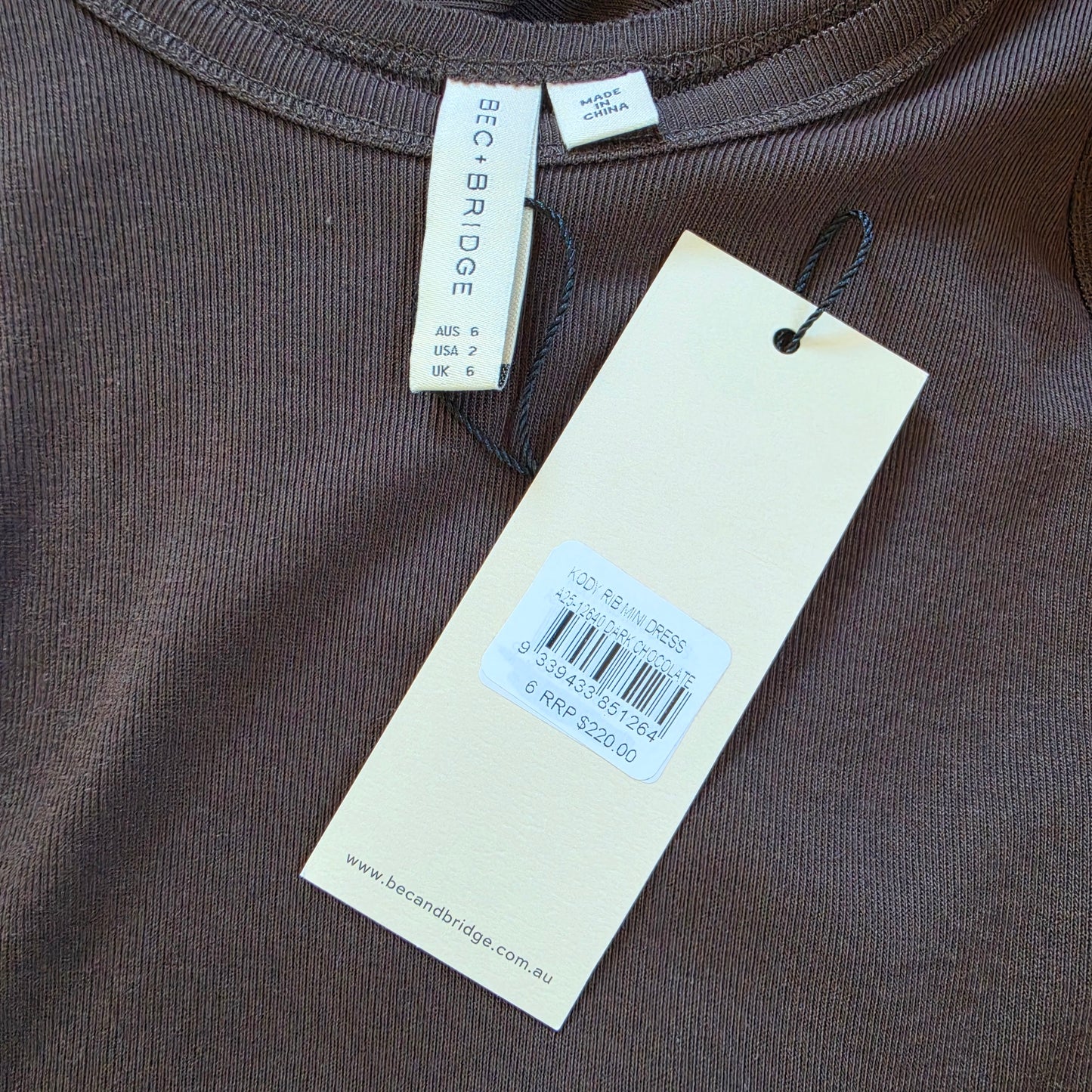 Image showing the swing tags on the Bec & Bridge Kody Ribbed Mini Dress, showing the size 6, rrp $220 and the colour as dark chocolate