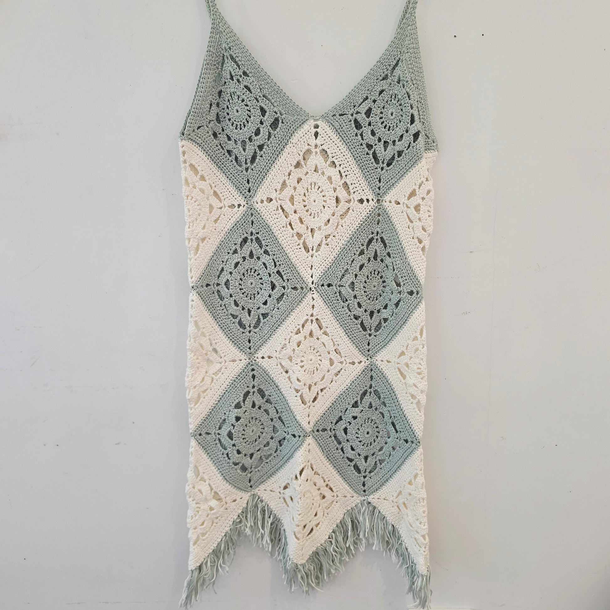 Flat lay of the crochet fringe dress in green & white with a fringe hemline.