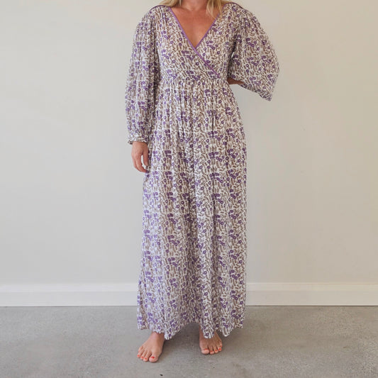 Front view of a woman wearing the Daughters of India long-sleeved Binita maxi dress with a purple and white abstract floral pattern and V-neck