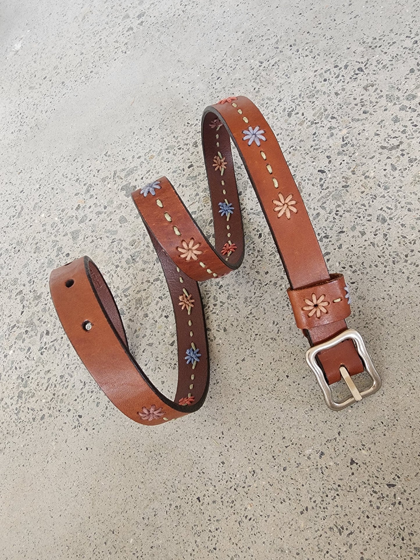 Close-up of Dockers leather belt showing stitched floral embroidery and buckle detail.