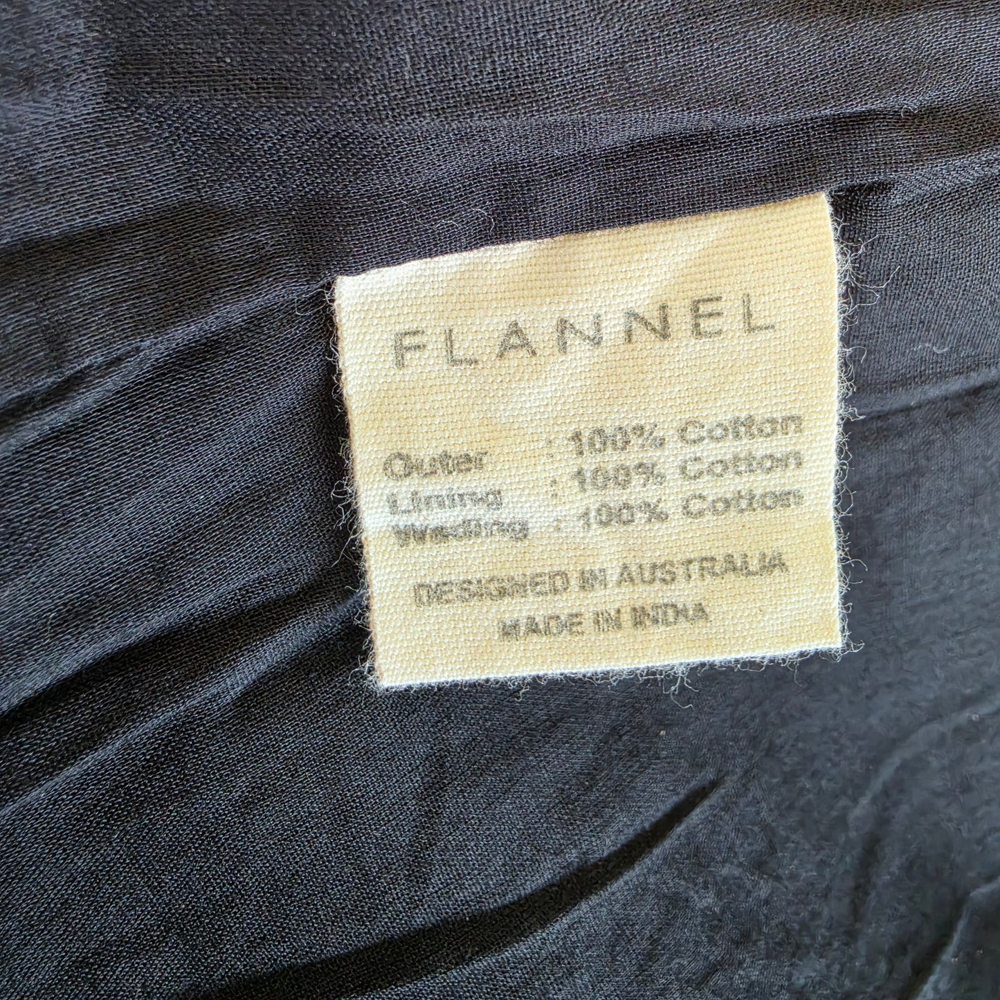Close-up of Flannel jacket fabric label showing 100% cotton and made in India.
