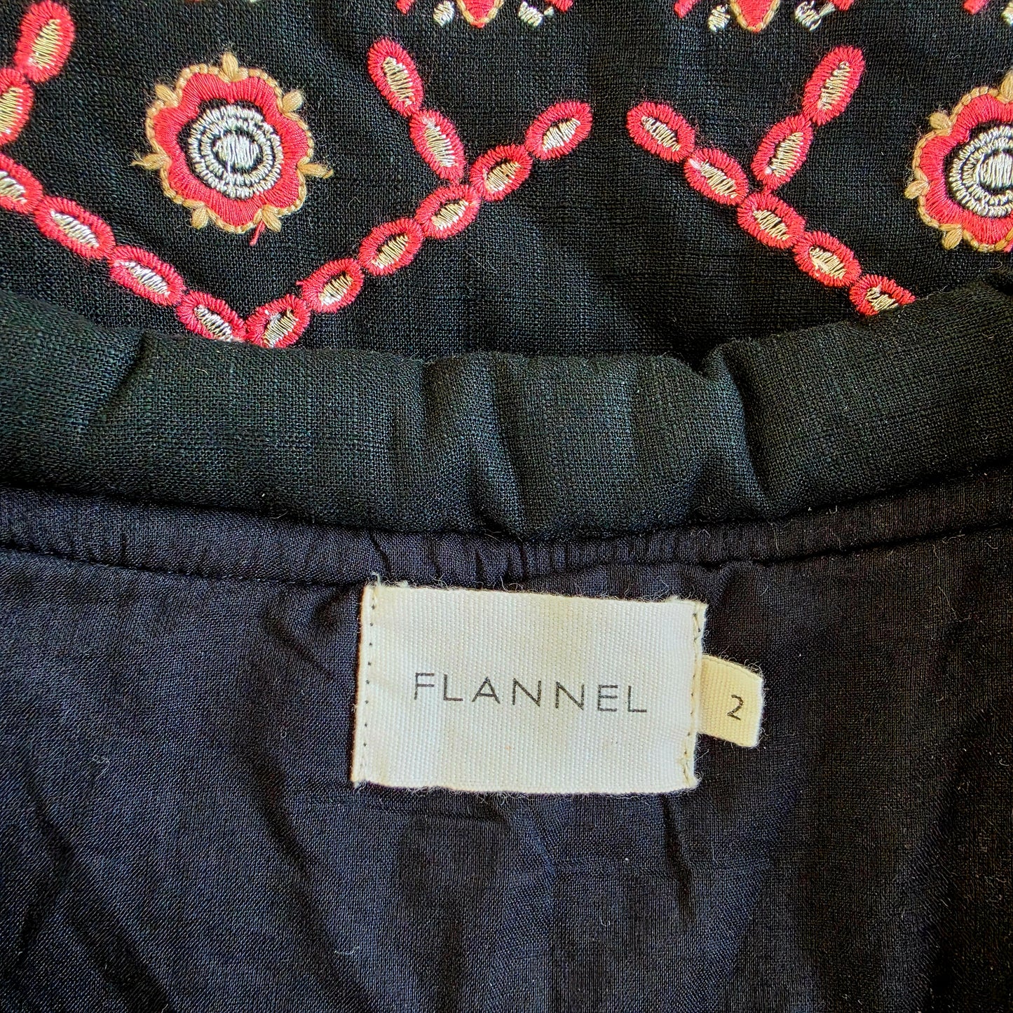 Flannel brand tag inside jacket with size 2 label, black lining and embroidered fabric visible.