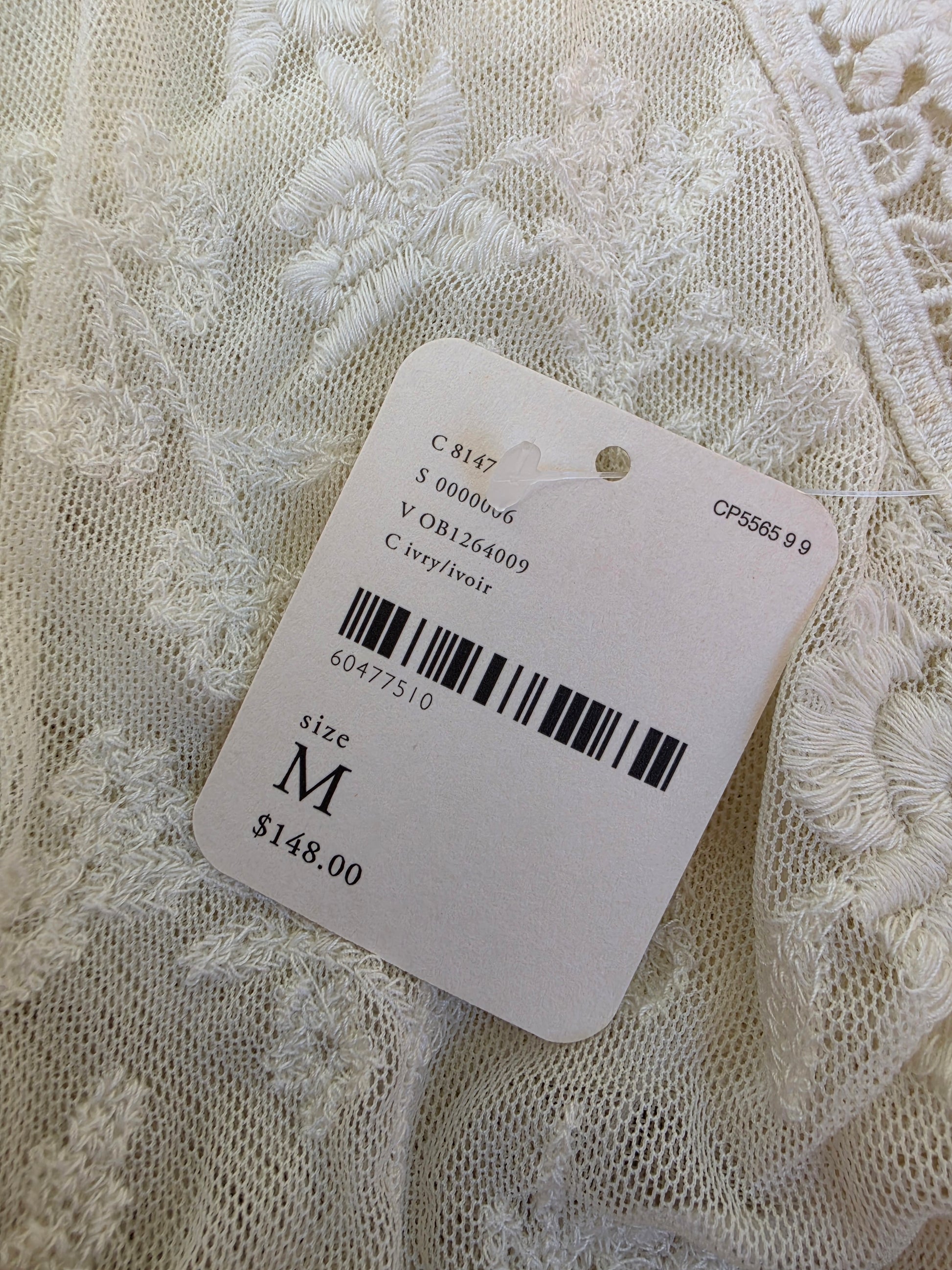 A close-up of white lace dress with a product tag attached, size M, and price $148.00.