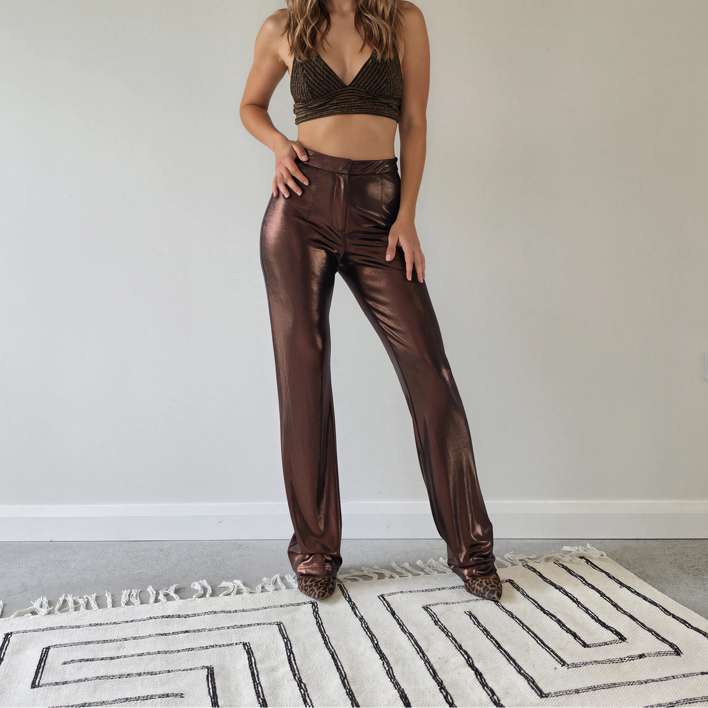 A woman wearing shiny metallic bronze Hansen & Gretel Bowie pants and a matching metallic bronze crop top.