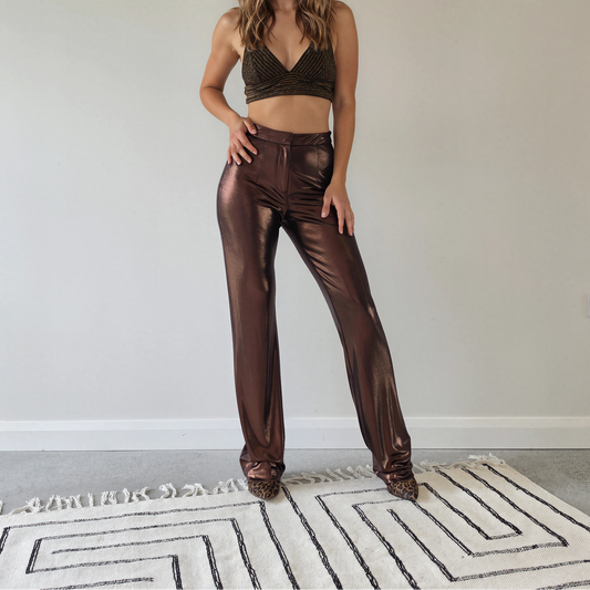 A woman wearing shiny metallic bronze Hansen & Gretel Bowie pants and a matching metallic bronze crop top.