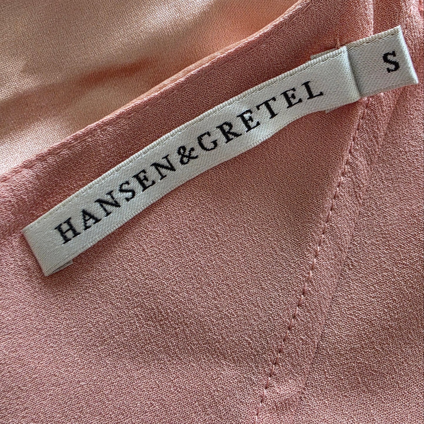 Close-up of the Hansen & Gretel blush slip dress with a white fabric brand tag reading HANSEN & GRETEL and size S.