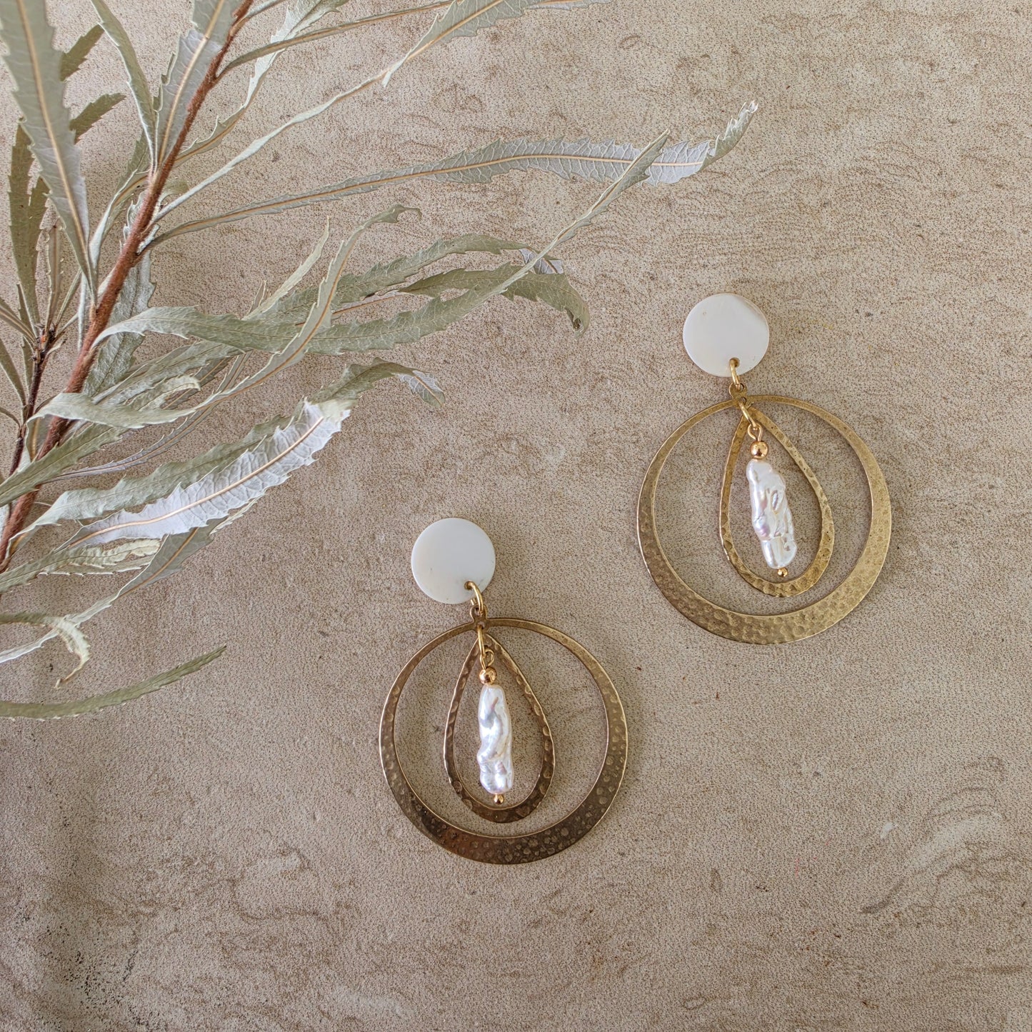 Top view of the Kolekti pearl earrings, showing the hammered brass, mother of pearl and gold plated components.