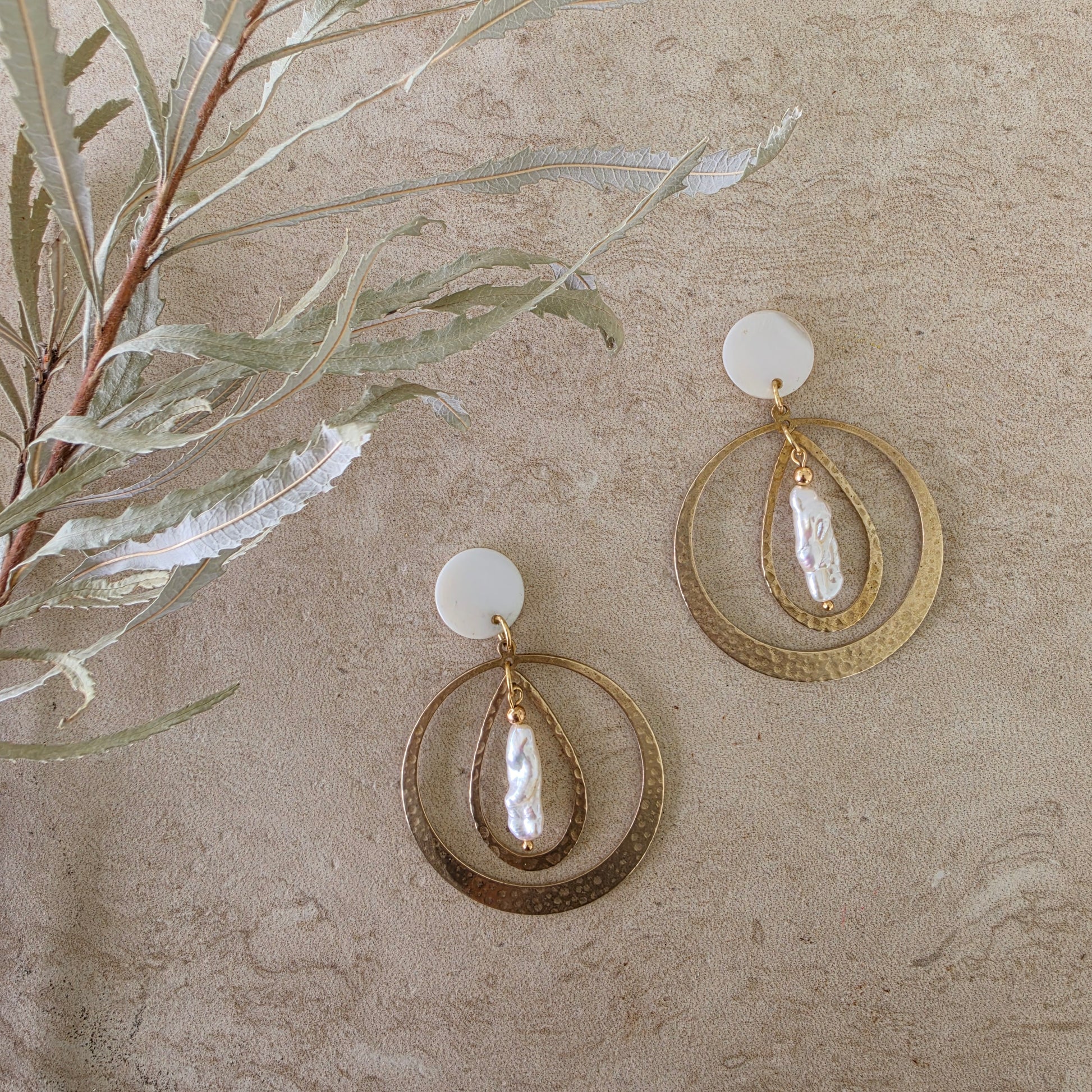 Top view of the Kolekti pearl earrings, showing the hammered brass, mother of pearl and gold plated components.