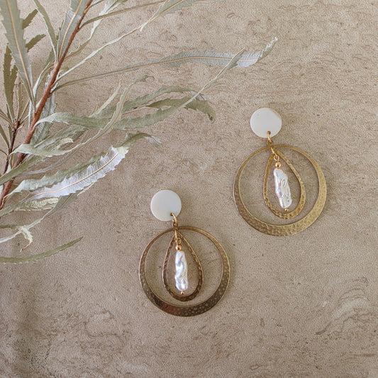 Top view of the Kolekti pearl earrings, showing the hammered brass, mother of pearl and gold plated components.