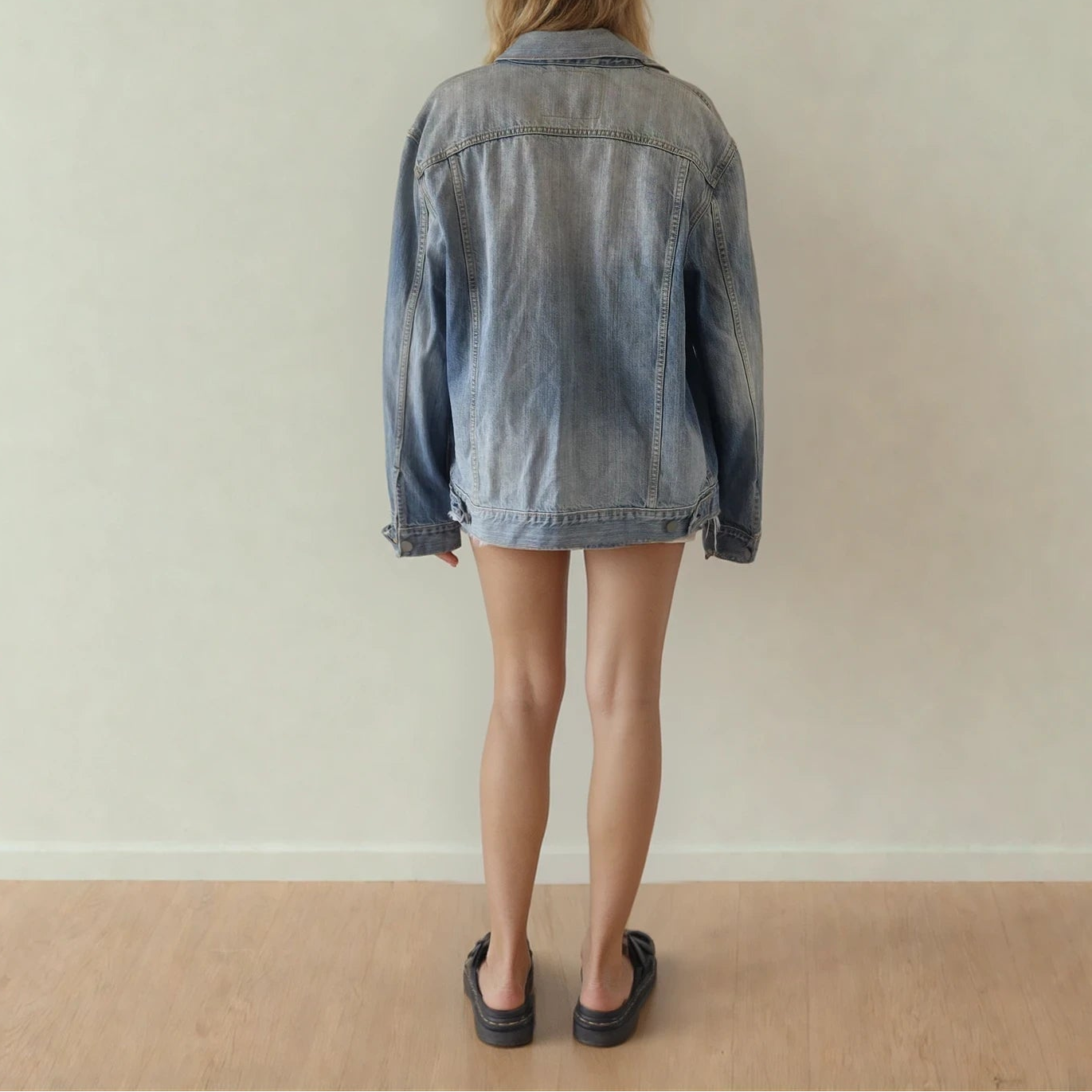 Image of the back of the Levis denim trucker jacket, showing the faded wash, and adjustable button details at hem.