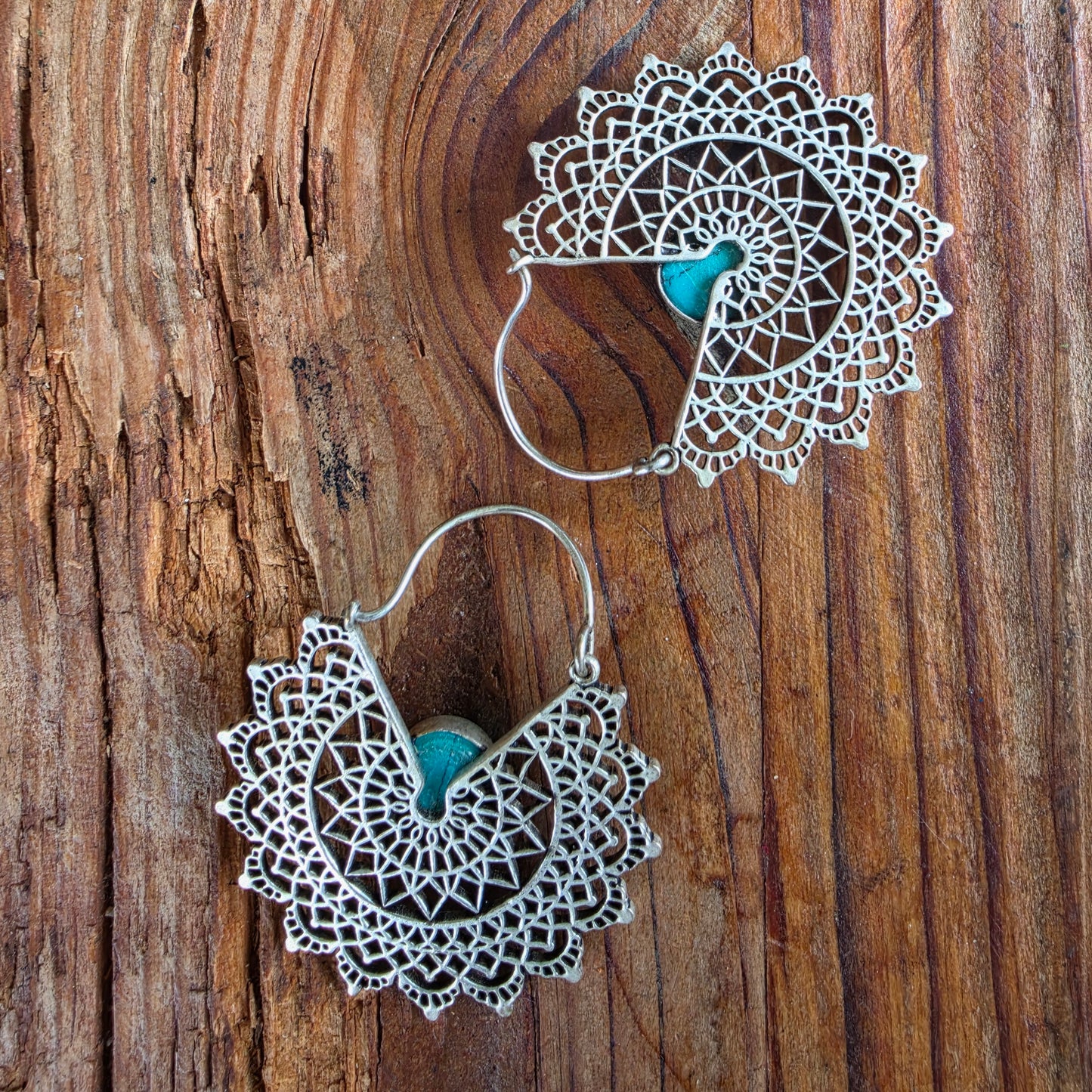 Back view of a pair of bohemian filigree earrings on textured wood surface