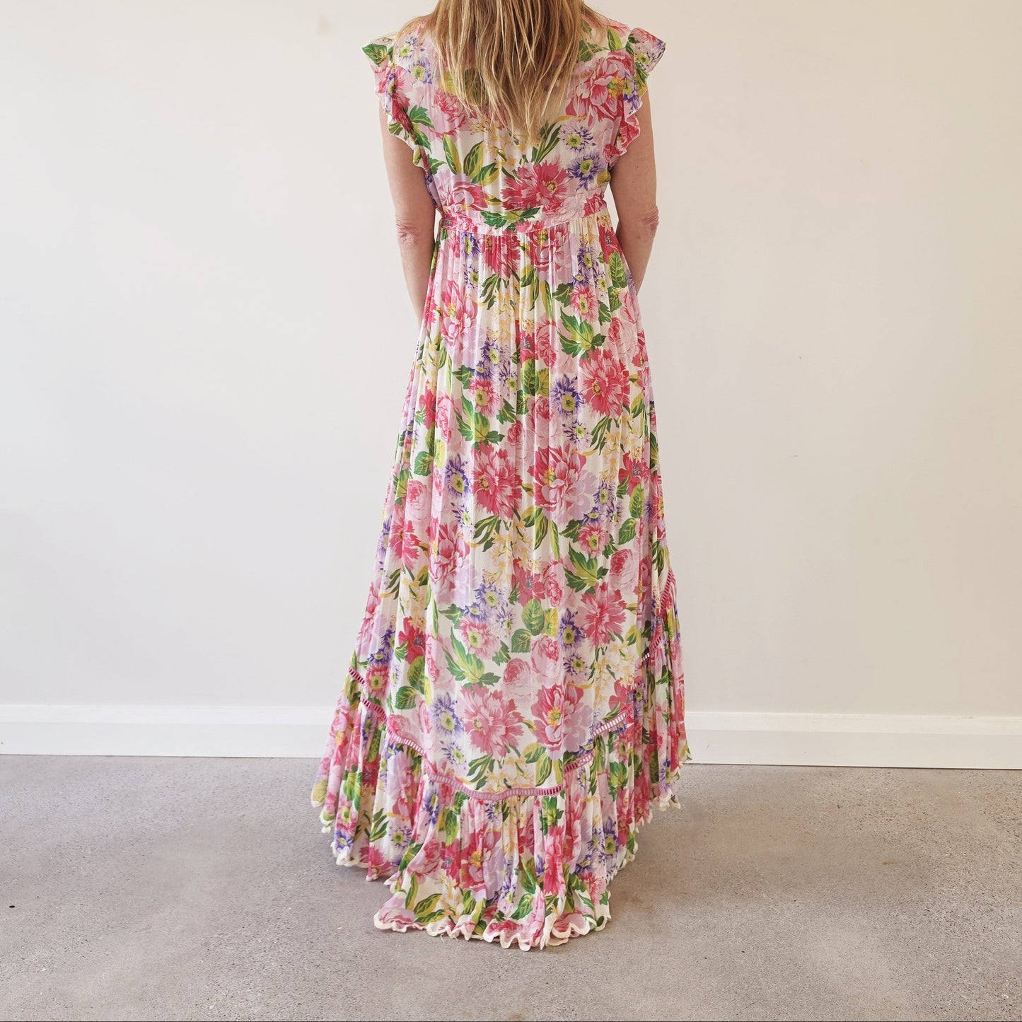 Back view of Miss June Paris Holly floral high-low maxi dress with flowing tiered skirt, ruffle sleeves and scalloped hemline.