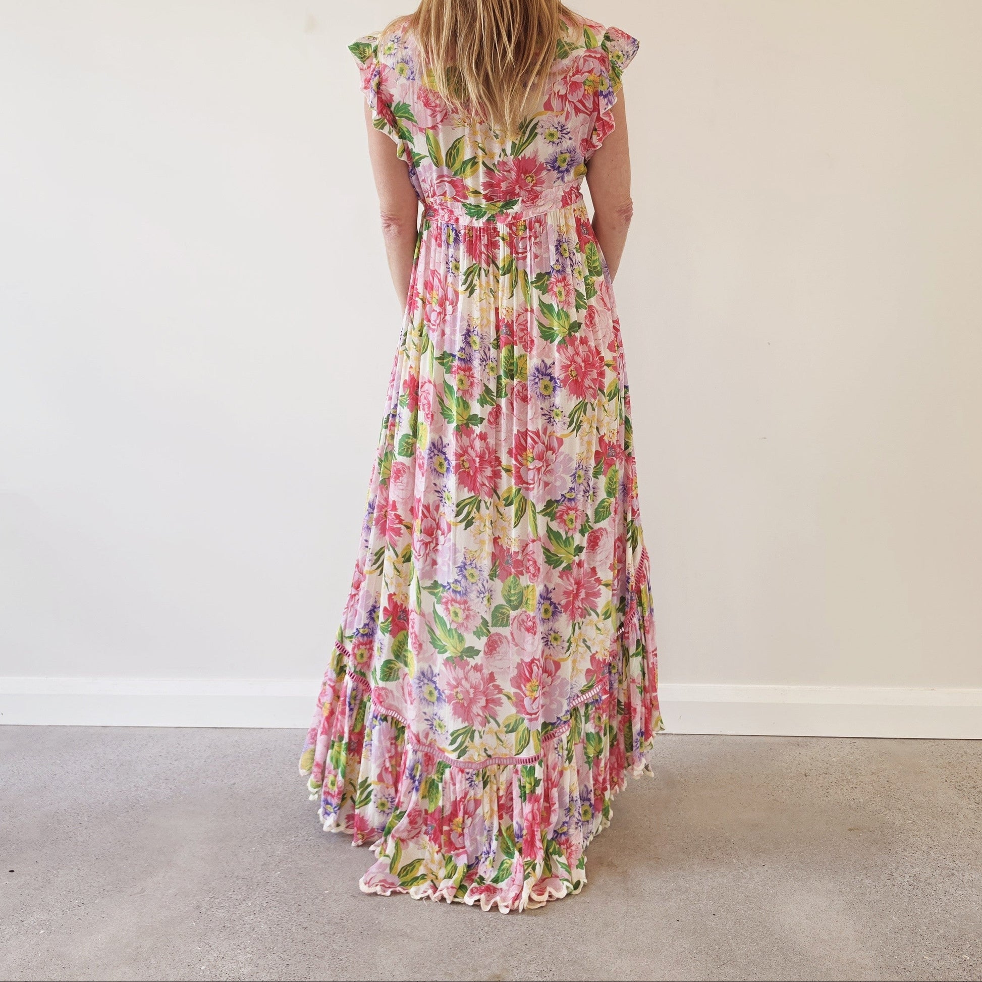 Back view of Miss June Paris Holly floral high-low maxi dress with flowing tiered skirt, ruffle sleeves and scalloped hemline.