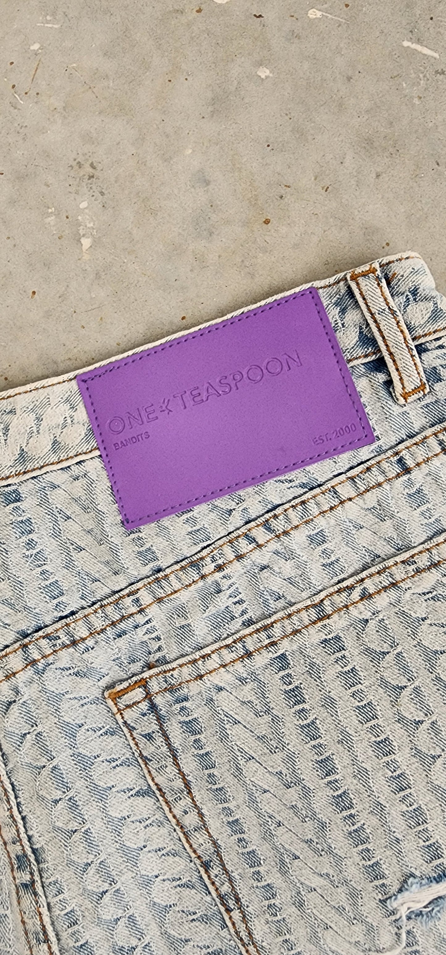 Close up image of the One Teaspoon bandit shorts, showing the exclusive print "on repeat", and the purple One Teaspoon back brand label.