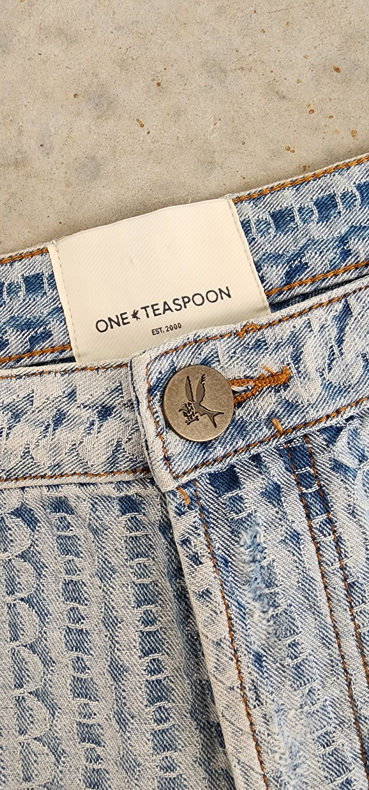 Close up image of the One Teaspoon bandit shorts, showing the exclusive print "on repeat", the One Teaspoon button and inside brand label.