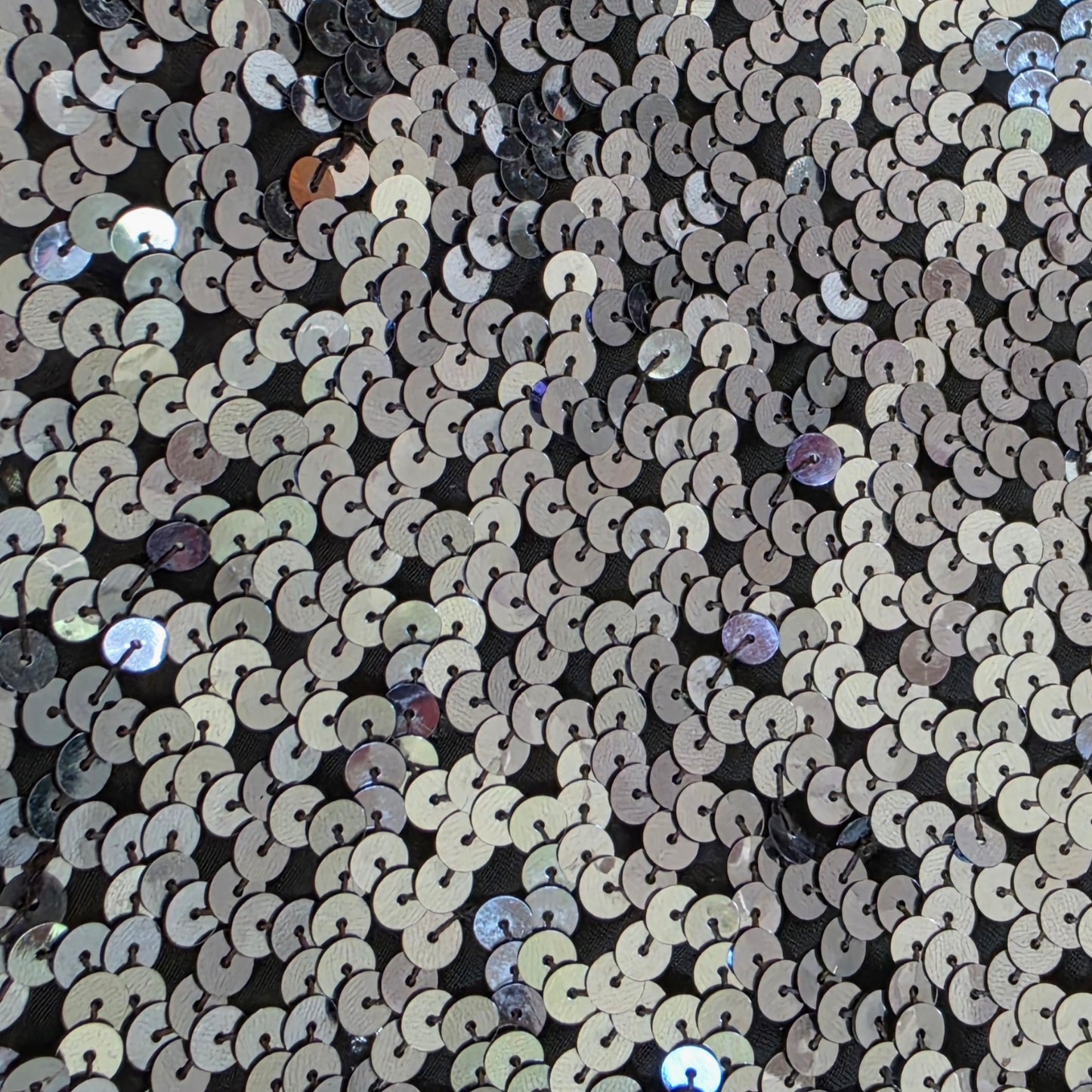 Close-up of sequin fabric with circular patterns in metallic colors on a black background