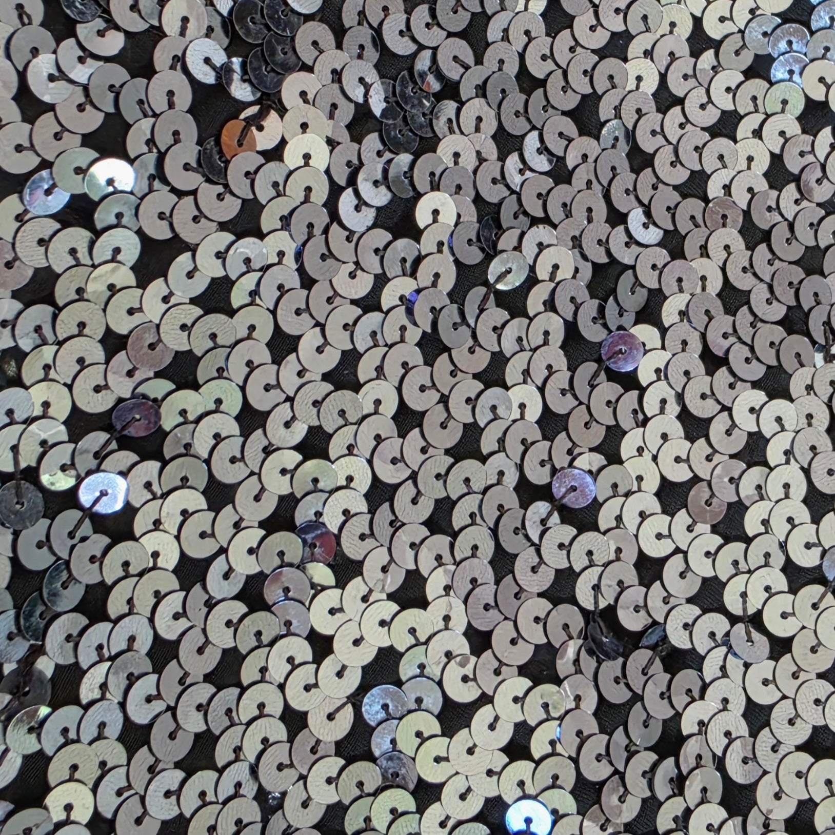 Close-up of sequin fabric with circular patterns in metallic colors on a black background