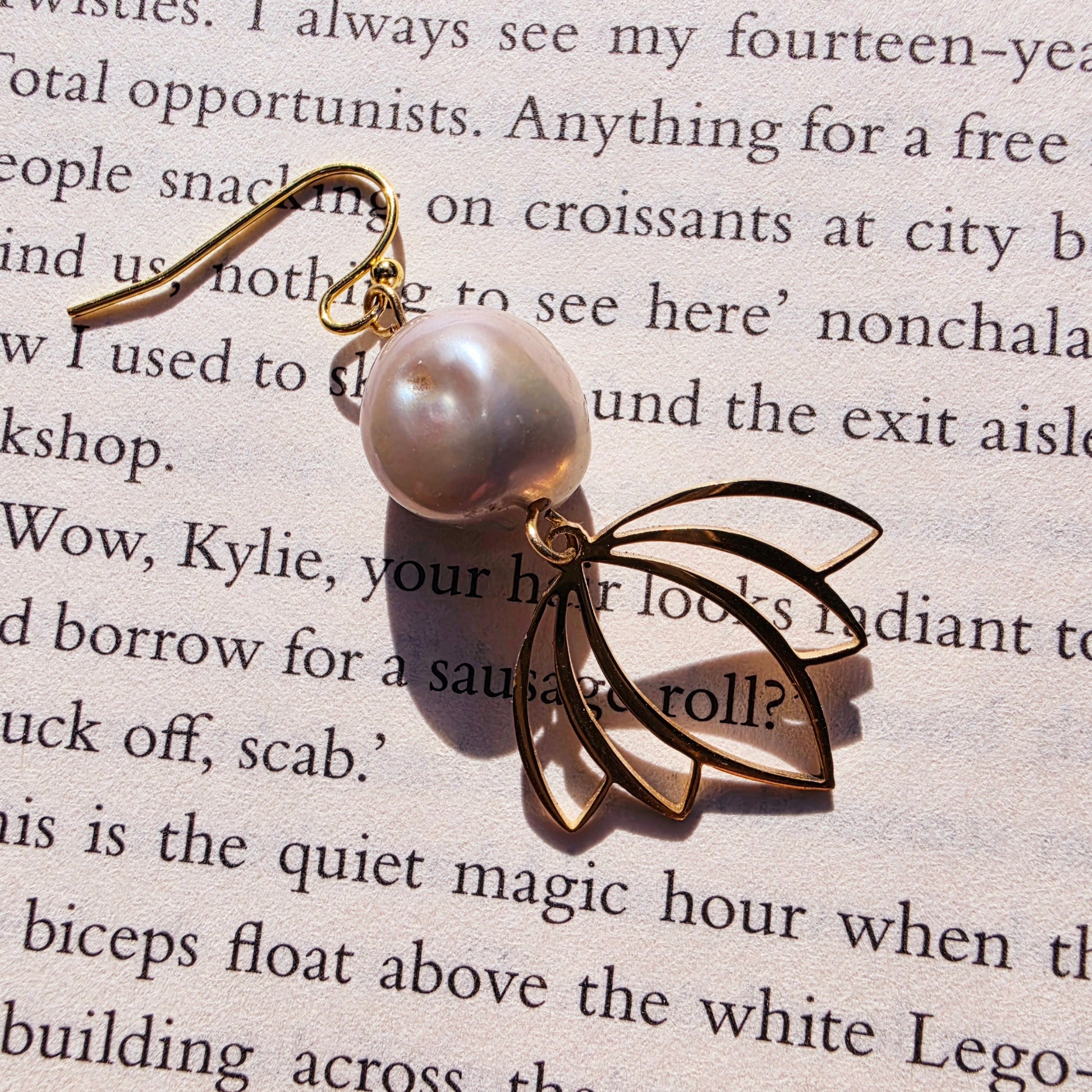 Close-up of baroque pearl drop earring with gold-toned hook showing the natural shape of the pearl and floral detail.
