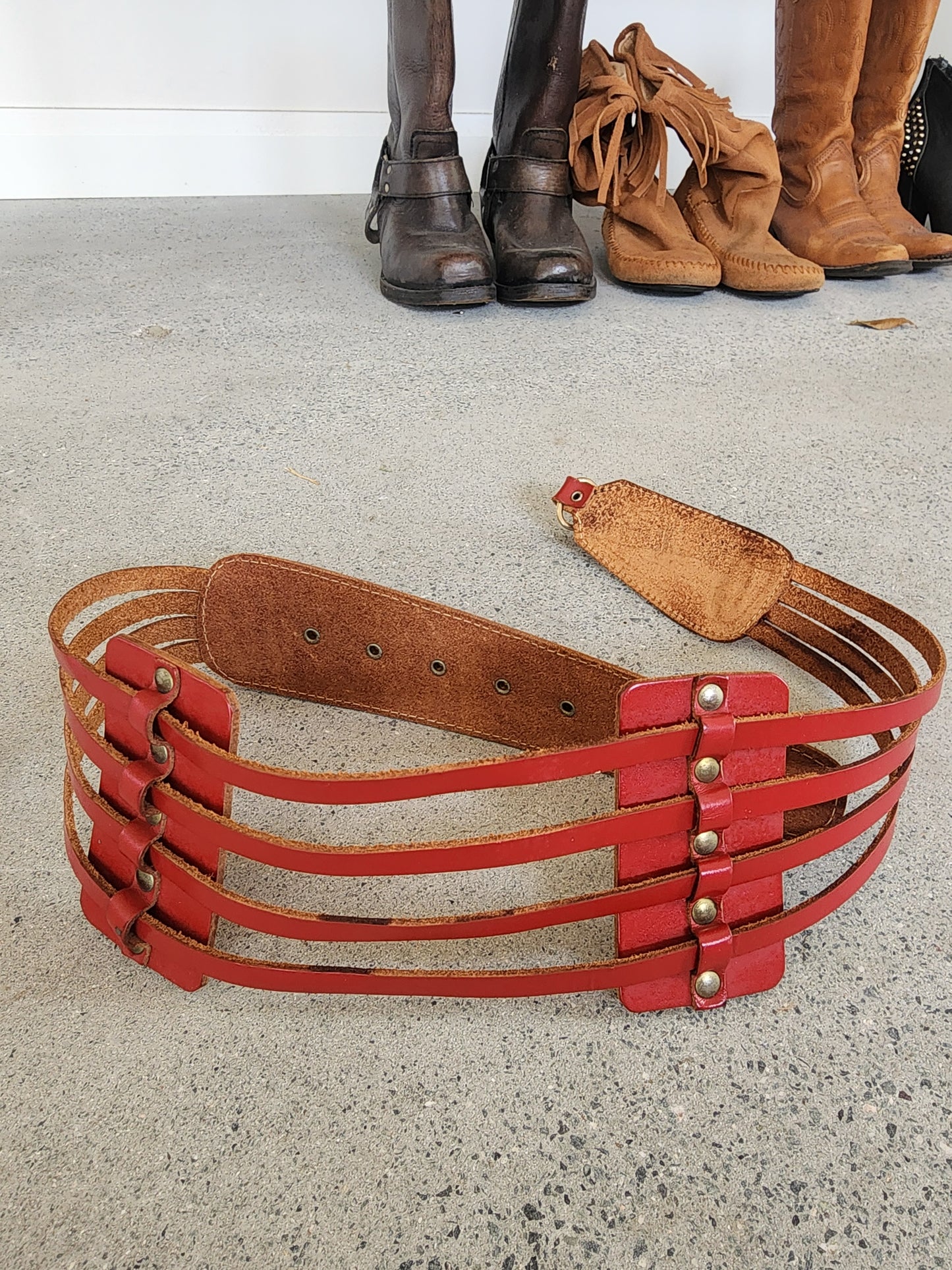 Close up of rouge red leather multi-strap waist belt with brass studs and clip fastening, raw leather backing.