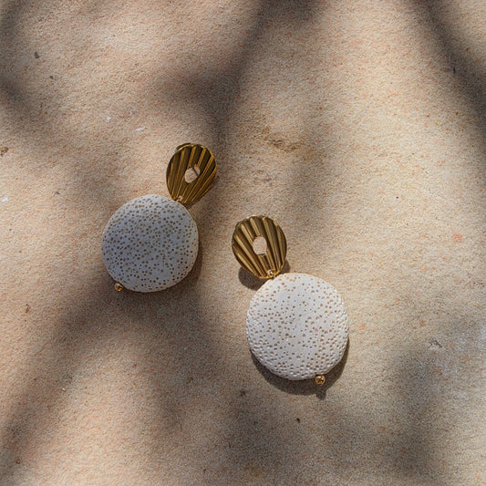 Flat lay of the Relic Lumen earrings in crema, showing the shell like stud clasp and textured surface of the bead