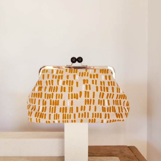 A retro clutch bag with a mustard line design displayed on a stand against a neutral background.