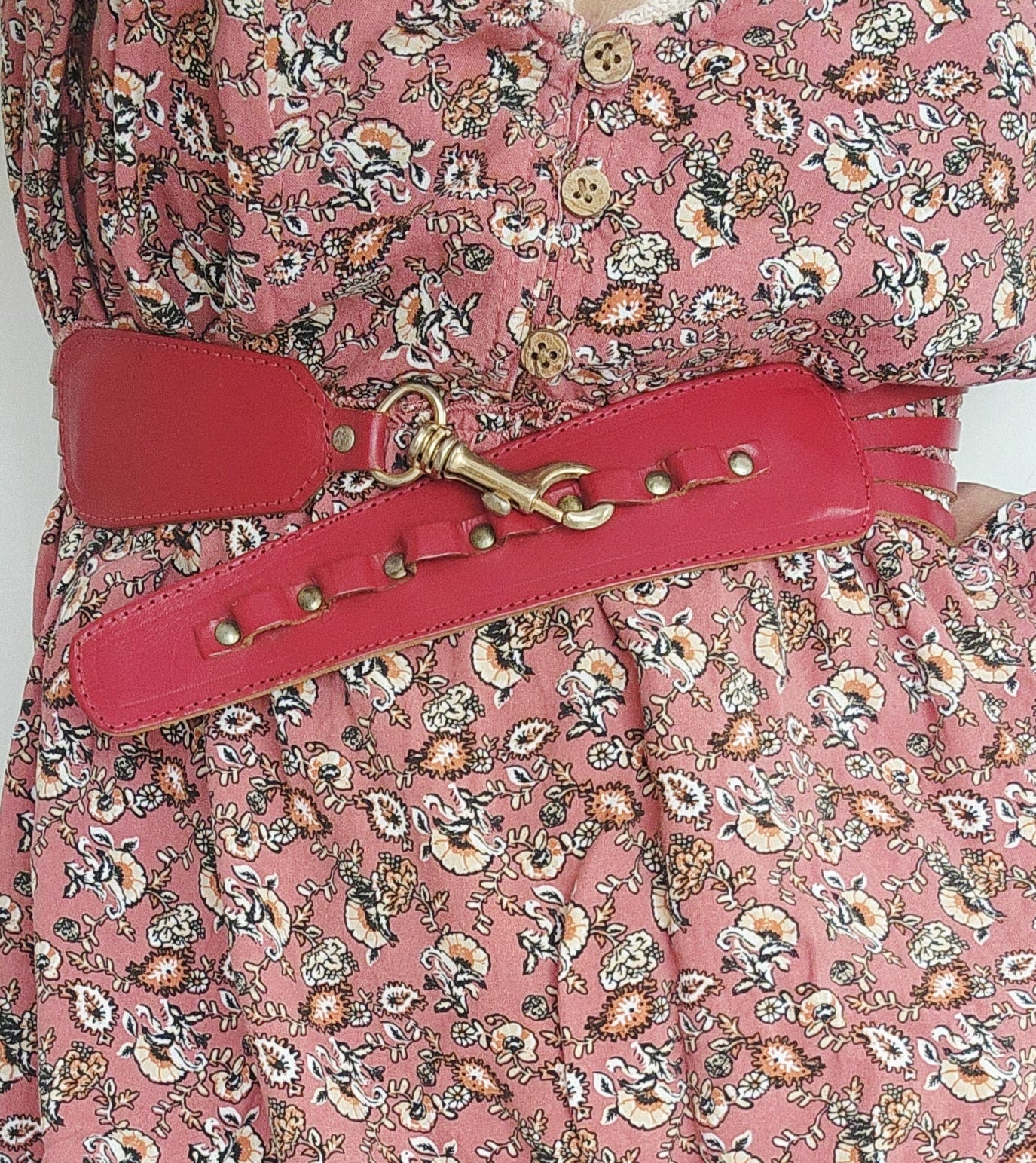 Rouge red leather multi-strap waist belt with brass studs and clip fastening, raw leather backing, styled over a pink floral dress.
