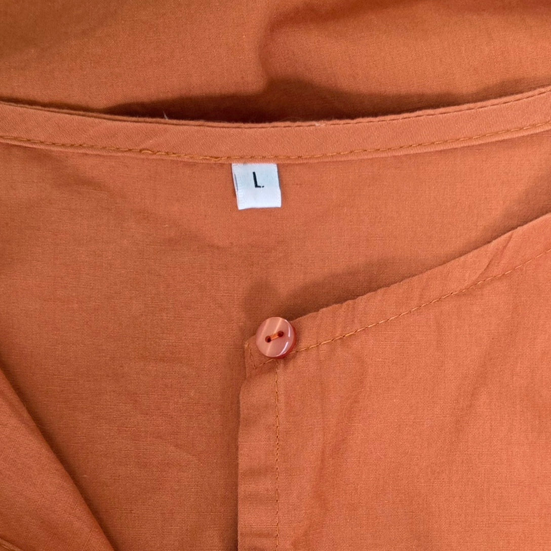 Close-up of a rust coloured shirt showing the inner collar with a white size tag marked 'L'