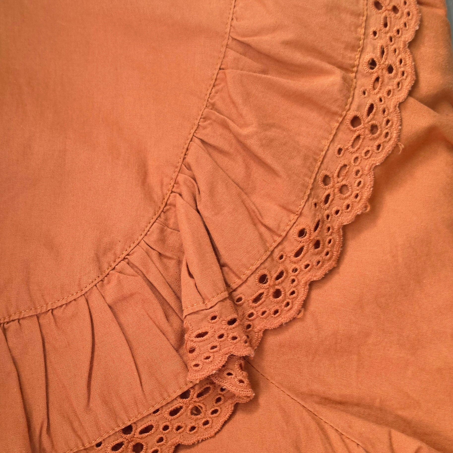 Close-up of the rust coloured blouse featuring a ruffled hem and eyelet lace trim.