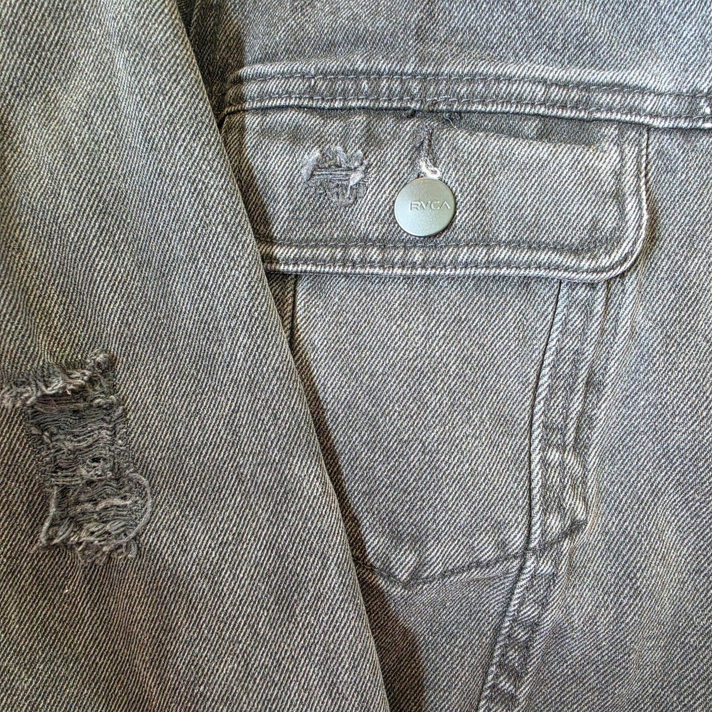 Close-up of distressed black denim jacket with frayed detail near pocket