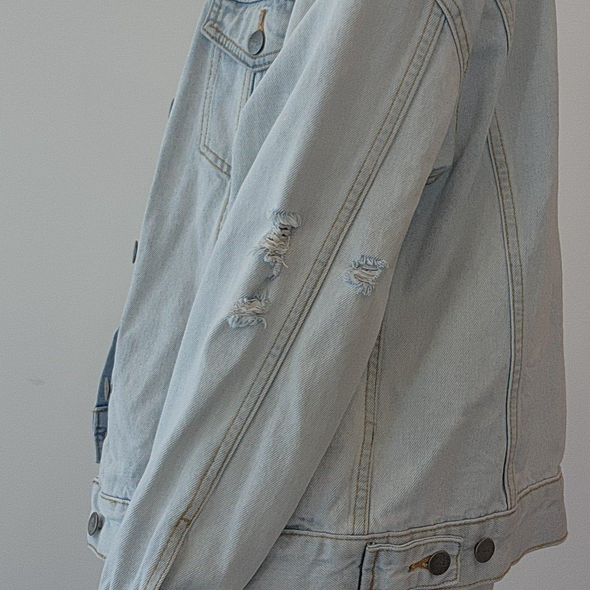 Side view of a model showing the factory distress on the RVCA light wash denim button up jacket.
