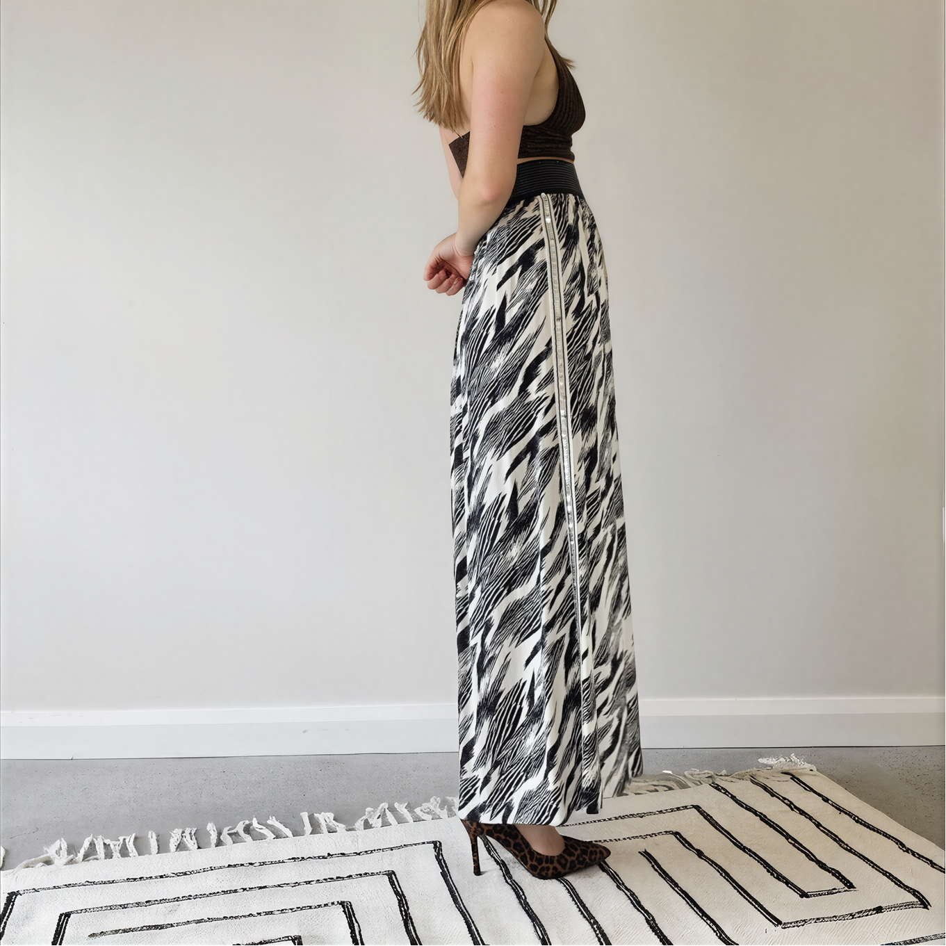 Side view of model wearing the Sass & Bide Bird of a Feather skirt, showing the monochrome print, sequin side panel, and wide metallic stripe waistband