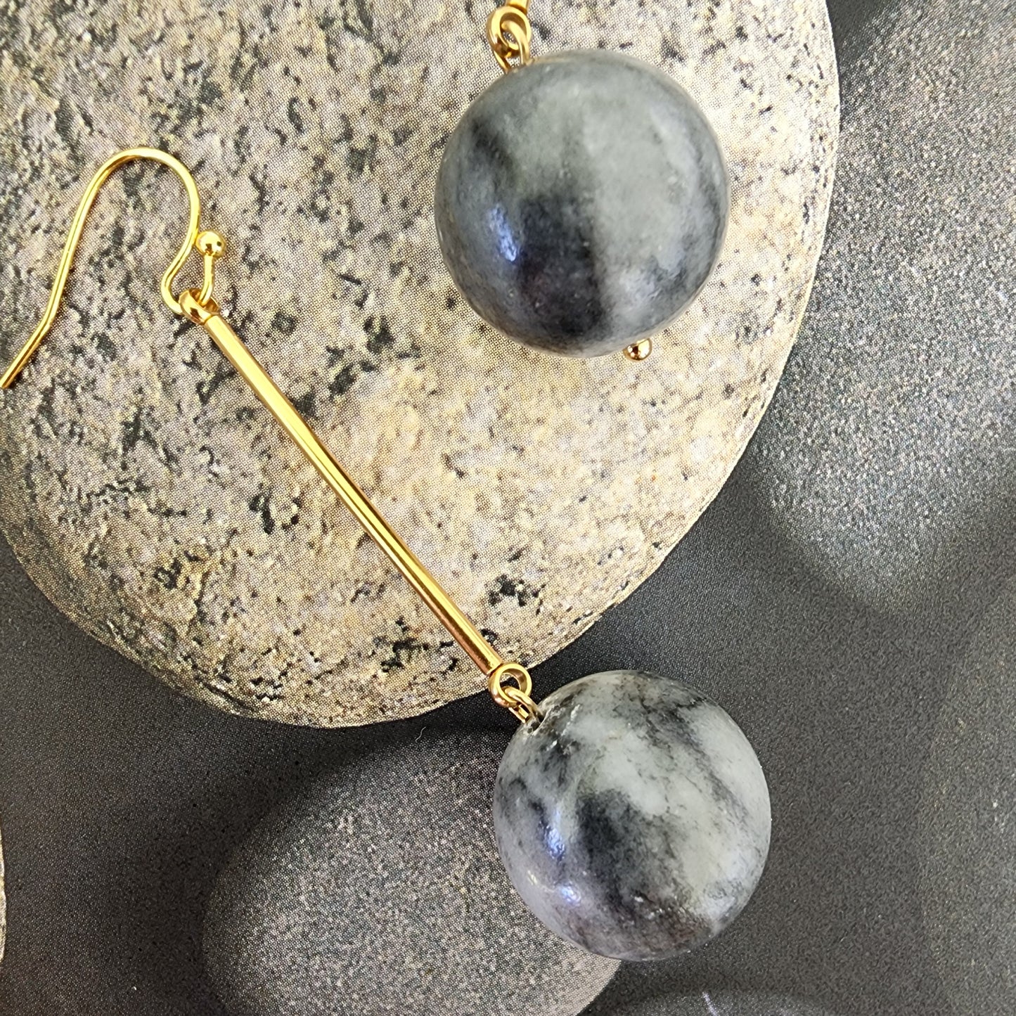 A close up image of the Shale handmade gold plated earrings, showing the variations in the globe shaped stone beads, suspended with gold plated components. A Wilson Avenue exclusive