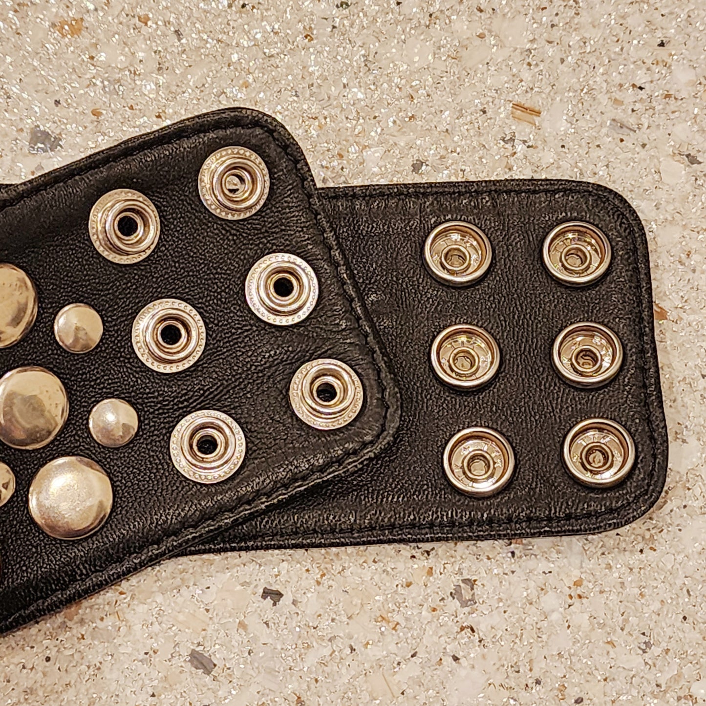 Close-up of Sirocco black leather belt with silver stud snap closure detail.