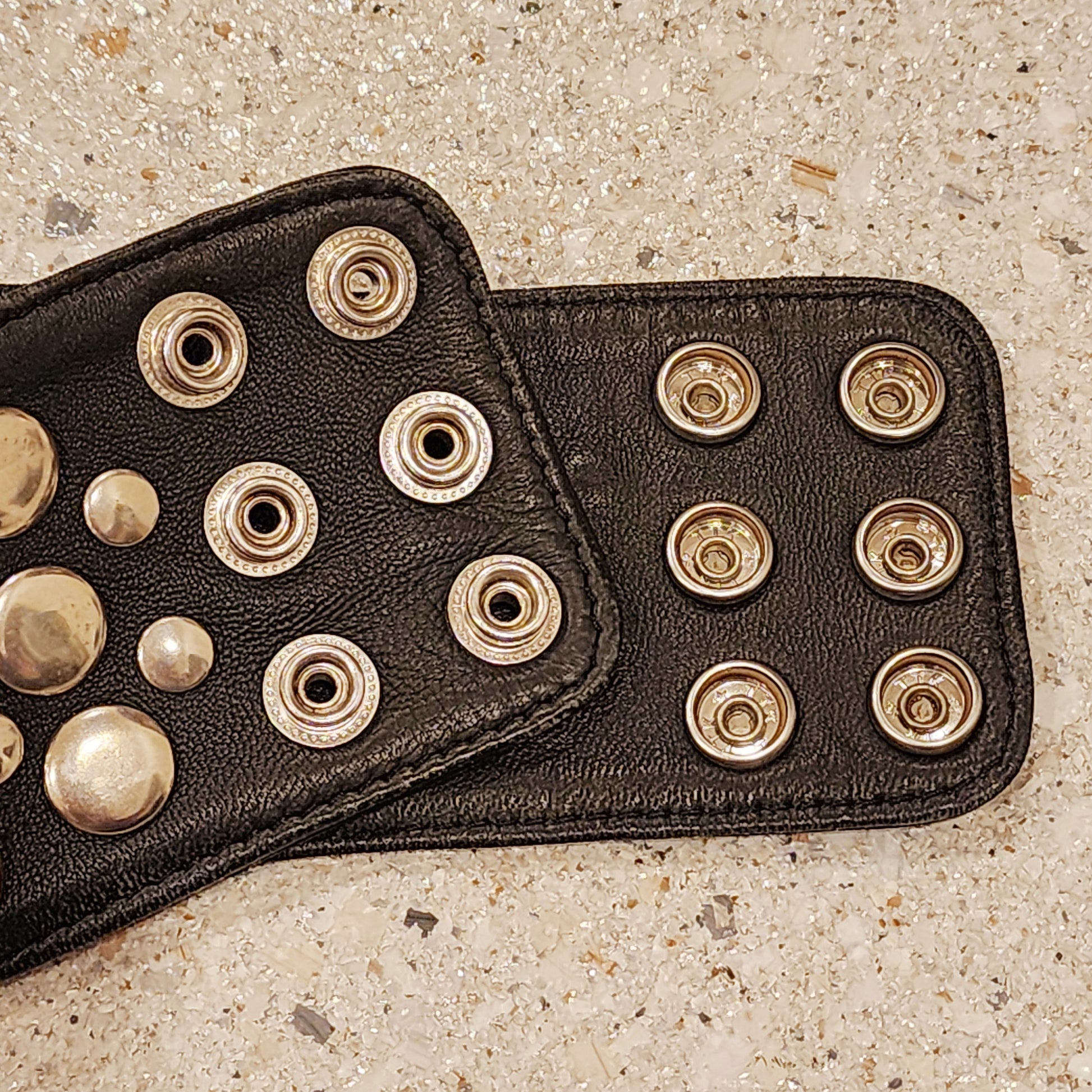 Close-up of Sirocco black leather belt with silver stud snap closure detail.