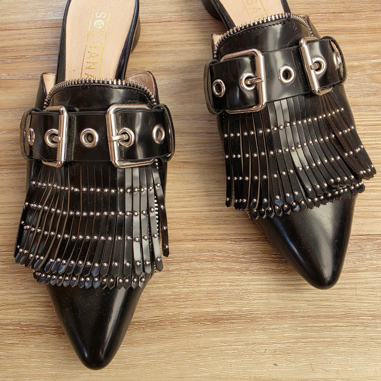Close-up of studded fringe, stud, buckle and zip detail on black leather Sol Sana Sadie slides