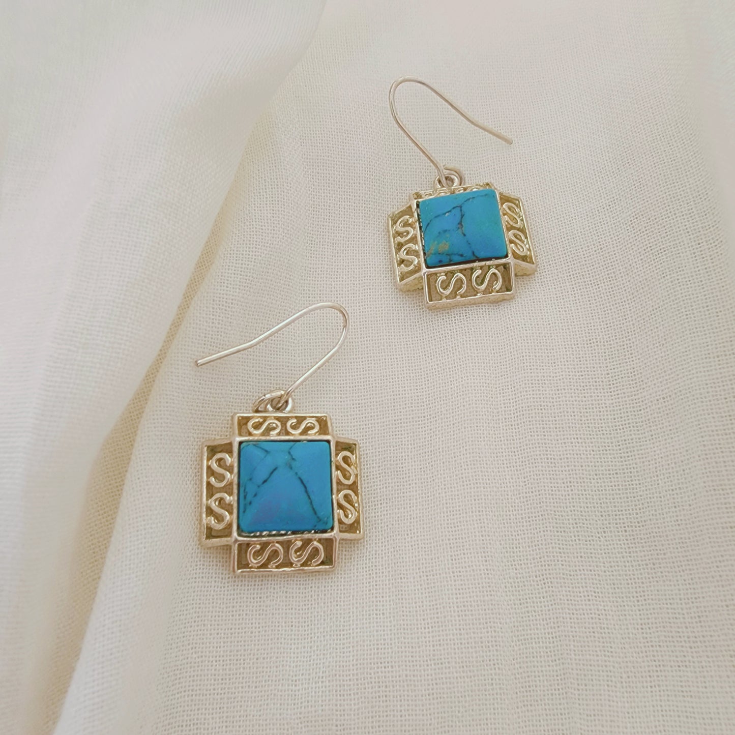 Sterling silver earrings with turquoise-coloured stones in a square setting, photographed on soft neutral fabric.