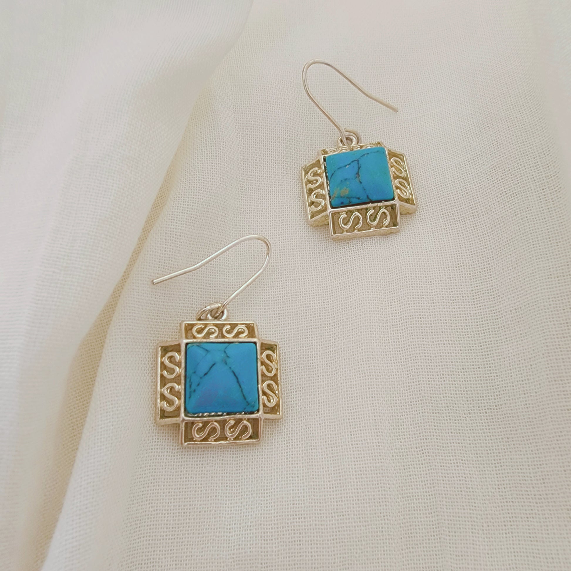 Sterling silver earrings with turquoise-coloured stones in a square setting, photographed on soft neutral fabric.