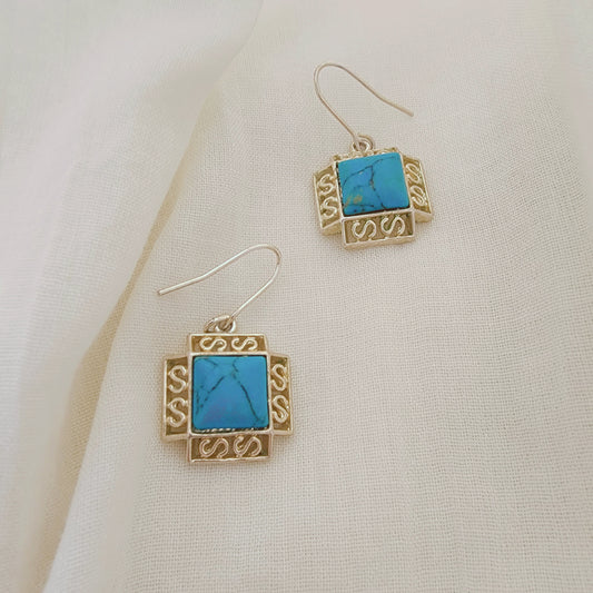Sterling silver earrings with turquoise-coloured stones in a square setting, photographed on soft neutral fabric.