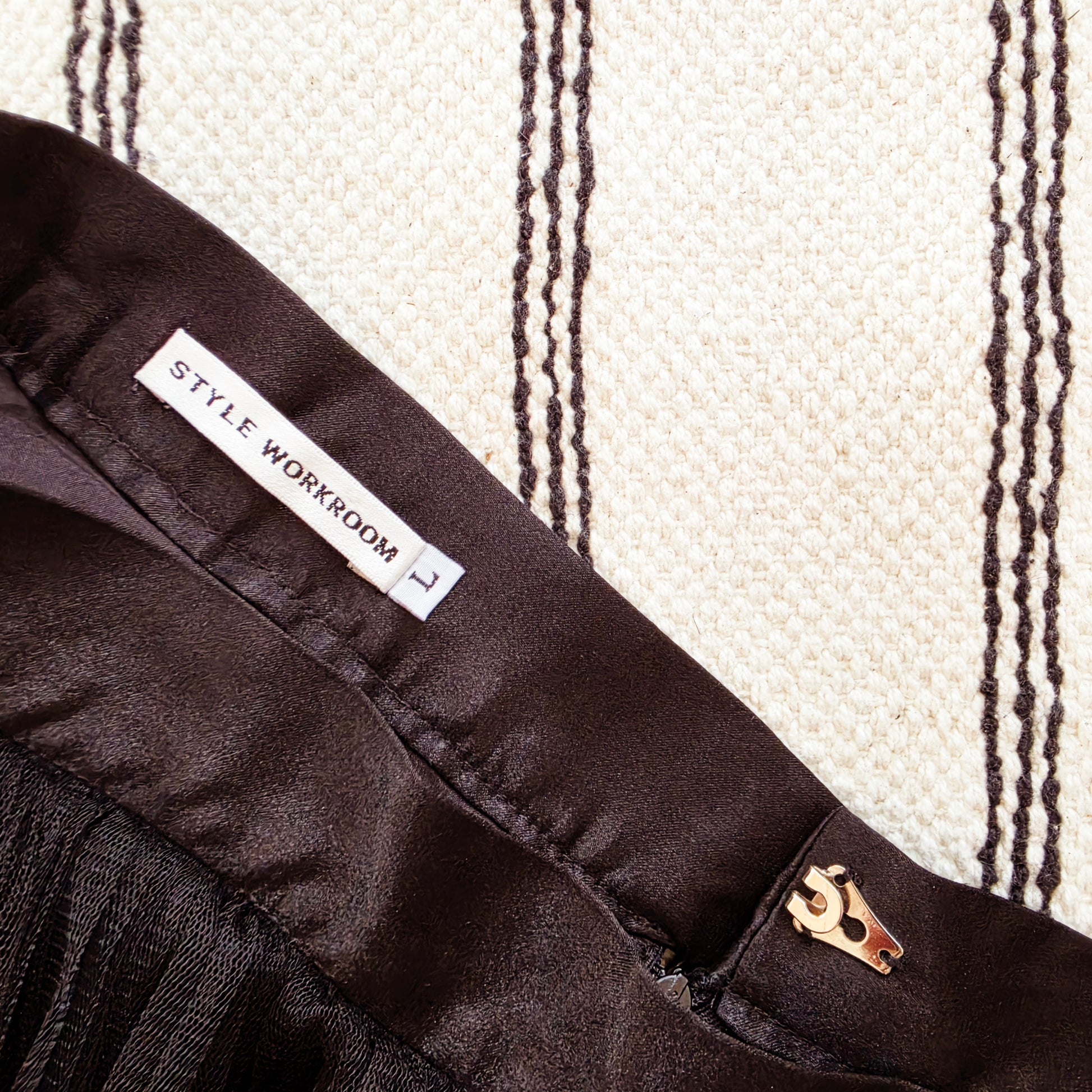 Close up of the inside waistband od the black Style Workroom tulle midi skirt, showing the brand label, size L and the slide clip clasp.